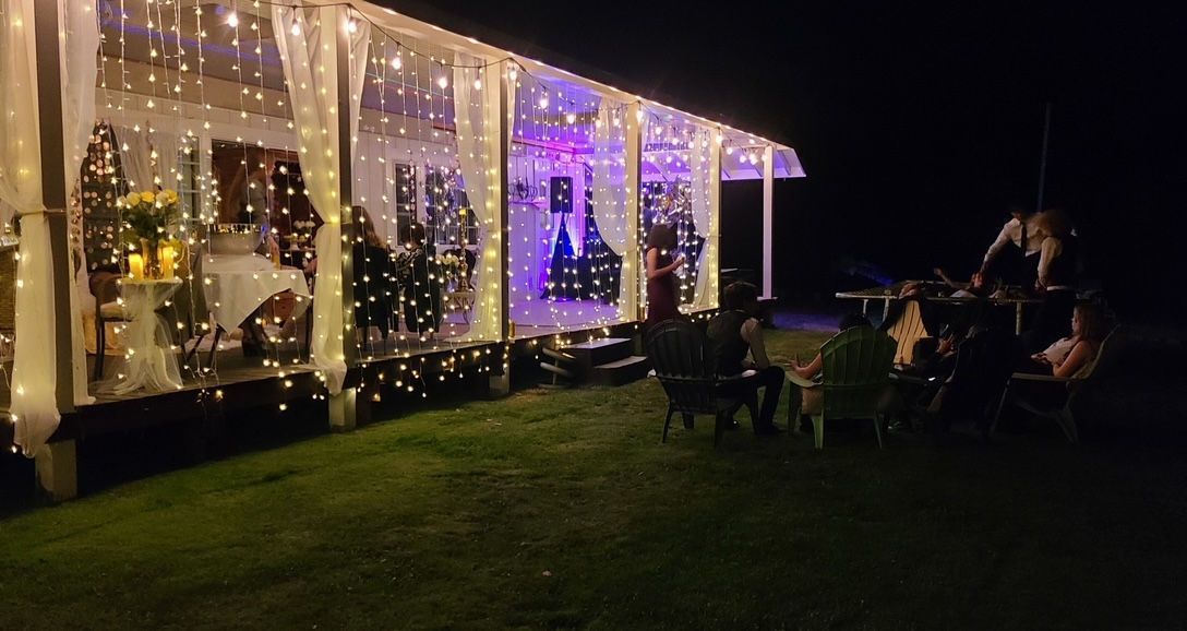 A porch decorated with lights, and people sitting in chairs in front of it at night.