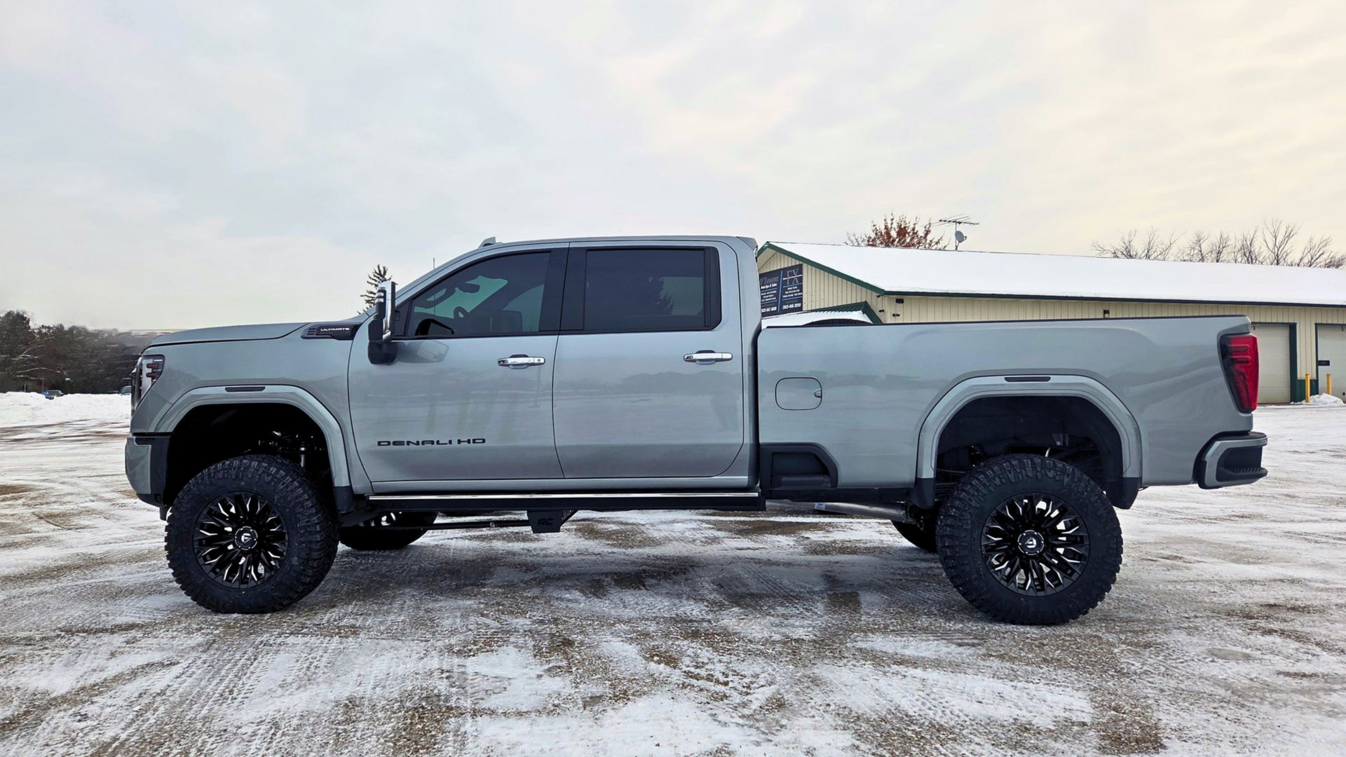 A silver lifted crew cab pickup truck parked in a snowy field.
