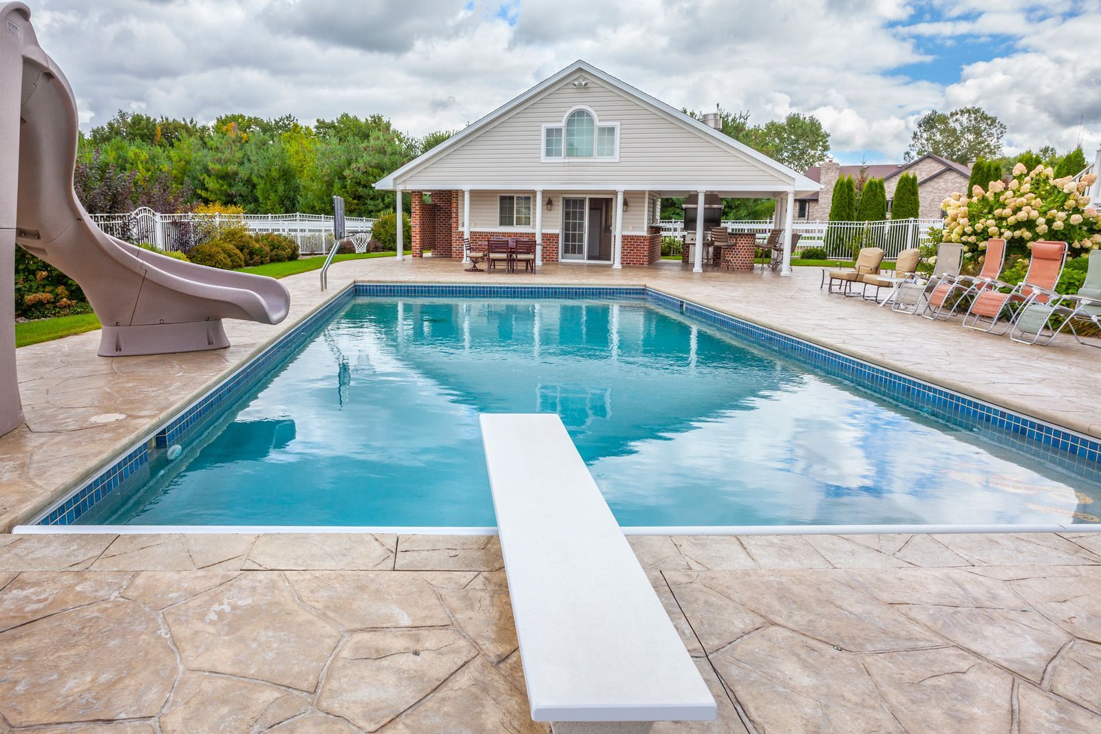 A large swimming pool with a slide and a diving board in front of a house.