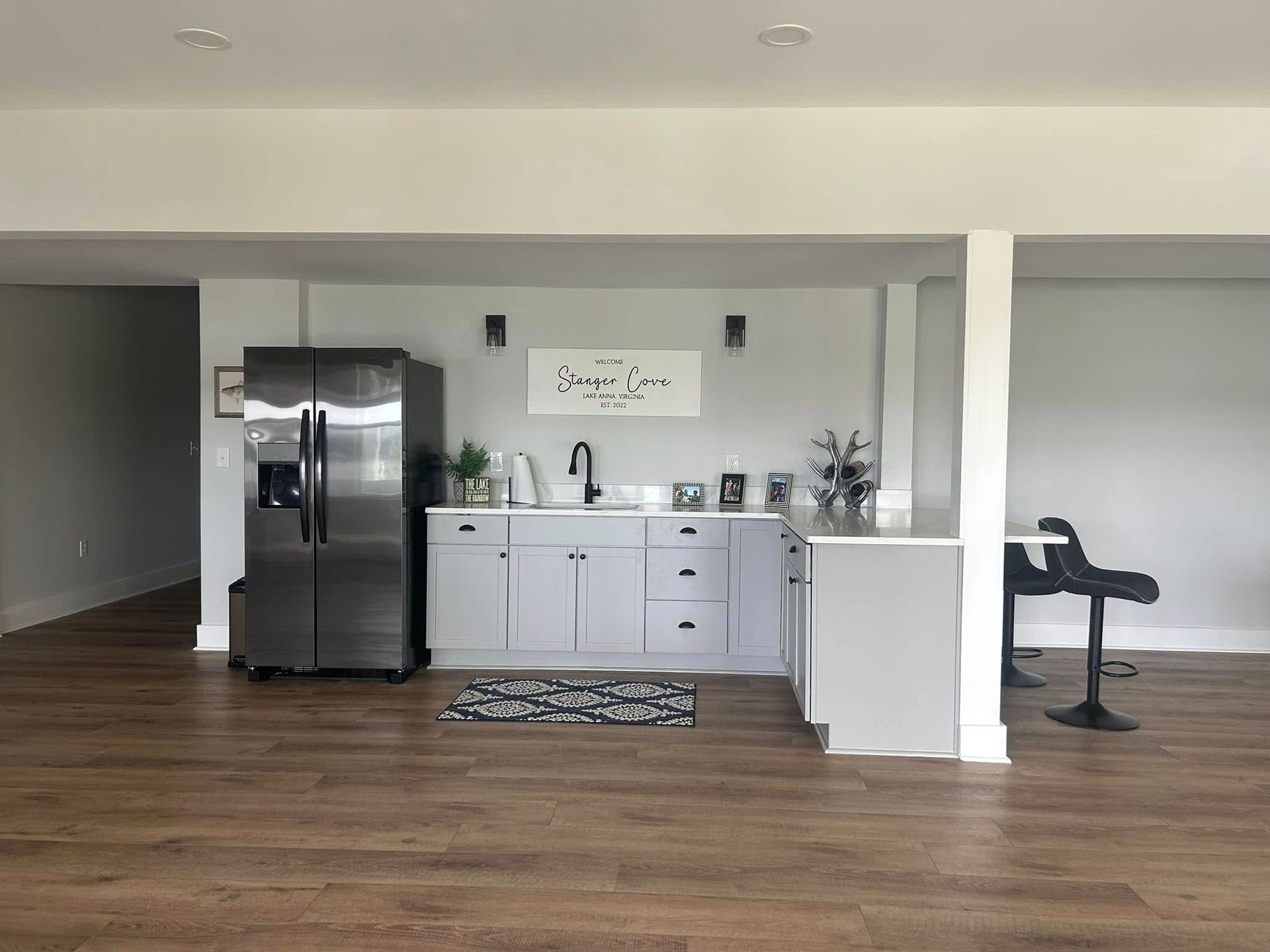 Open kitchen with stainless steel fridge, white cabinets, island, and hardwood floors in a modern home.