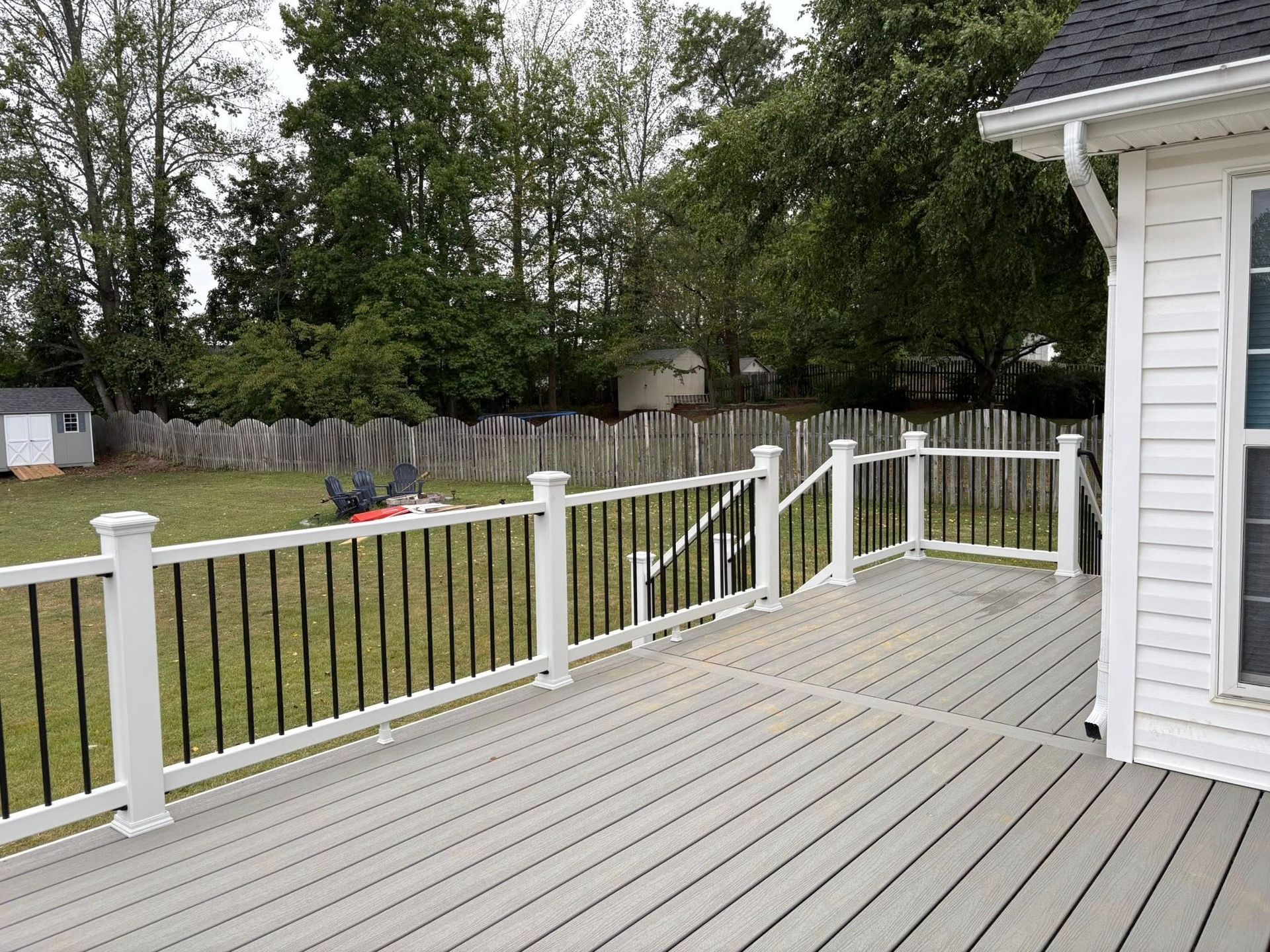 White deck with railing beside a house, overlooking a grassy yard and trees