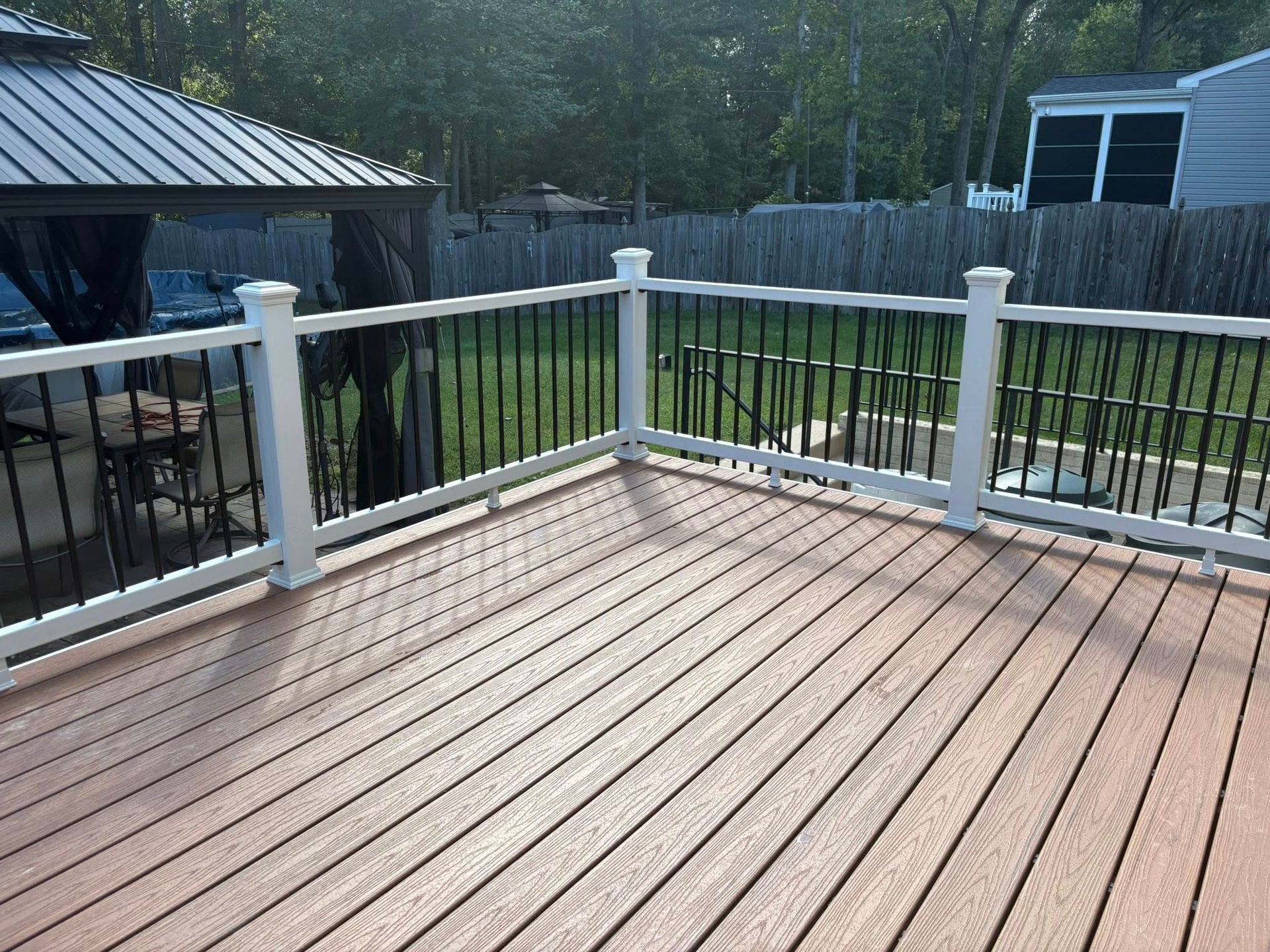 Wooden deck with white railing and fenced backyard, viewed from a corner in daylight