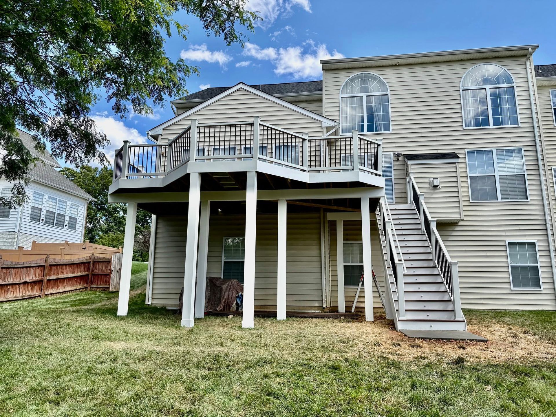 Raised backyard deck with stairs and lattice under a beige house, viewed from the lawn