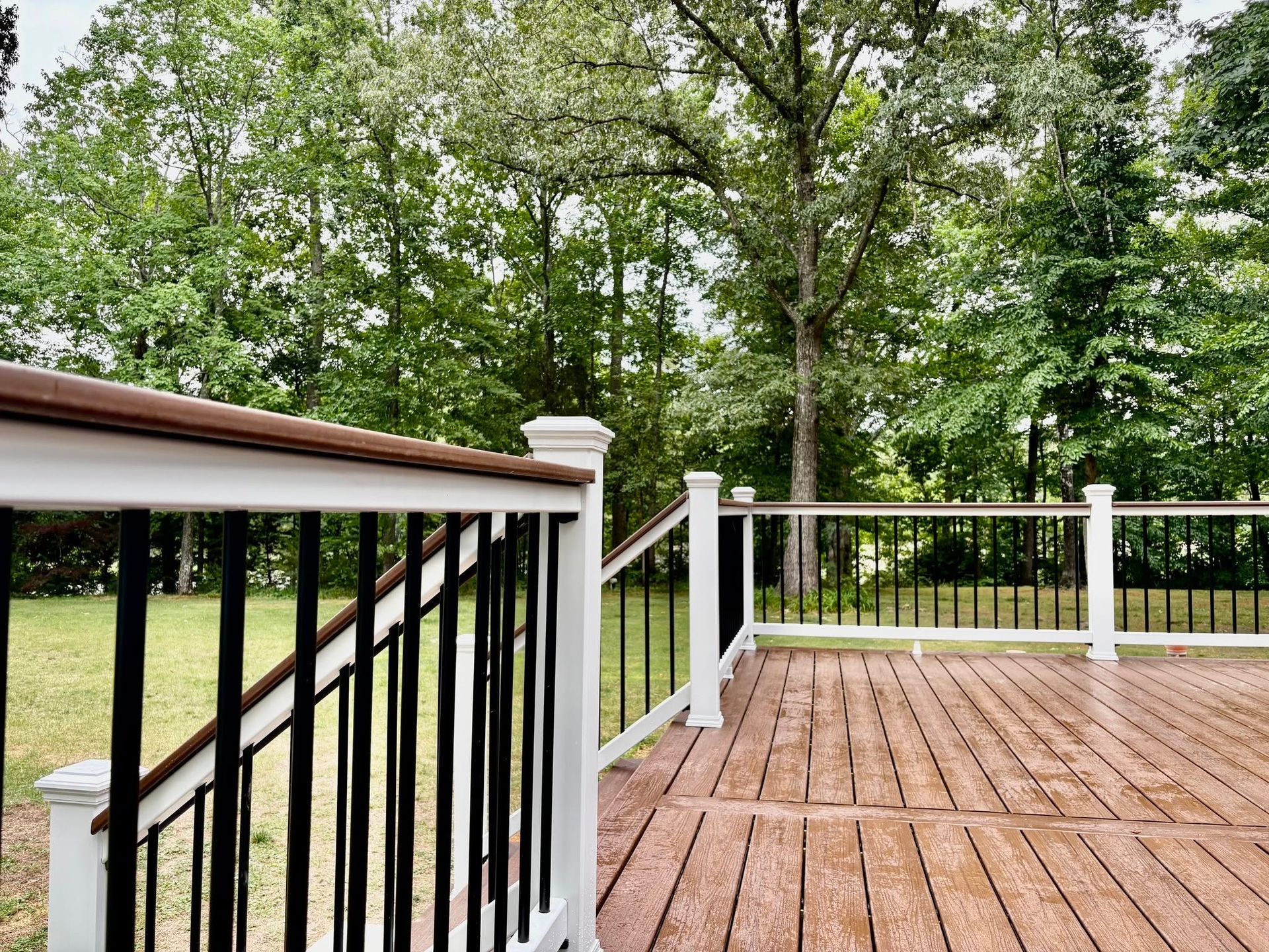 Wooden deck with black-and-white railing overlooking a green backyard and trees