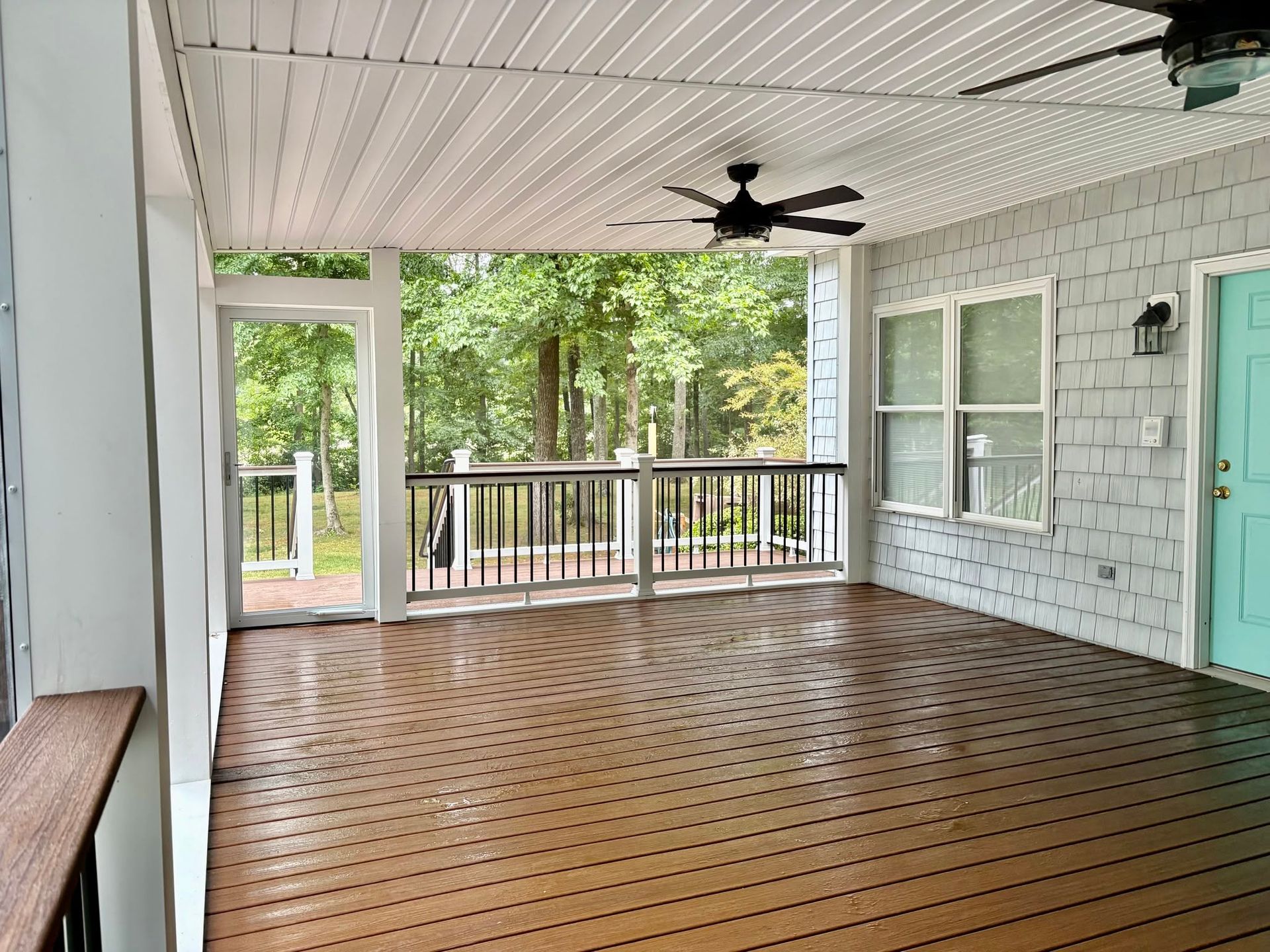 Covered porch with wood floor, white ceiling, ceiling fan, railing, and turquoise door.