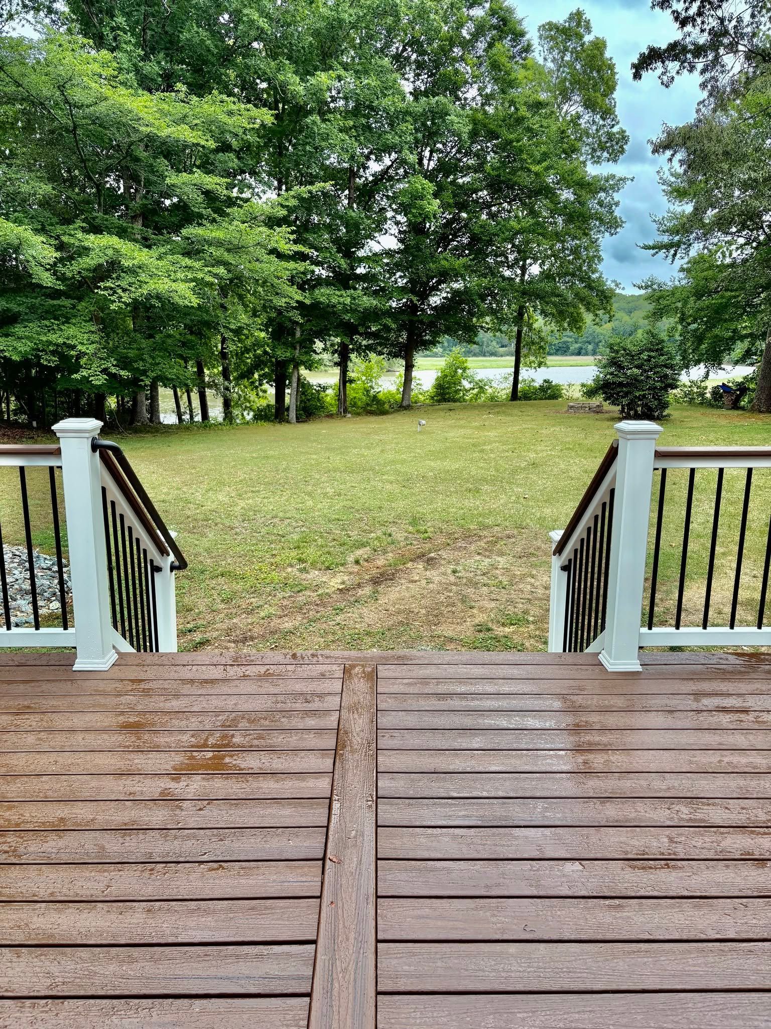 Wooden porch steps overlook a grassy yard with trees and a distant lake.