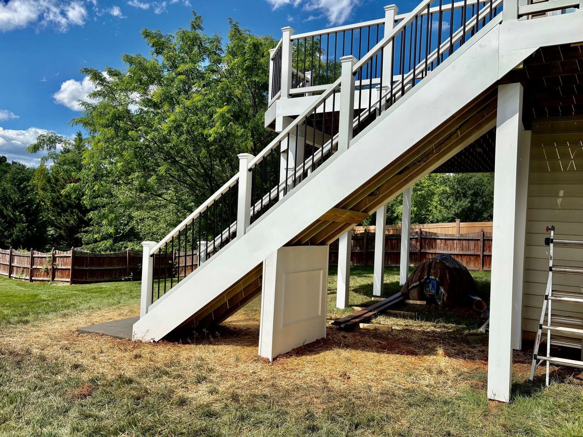 Backyard staircase leading to an elevated deck, with white railings and wooden steps over dry grass.