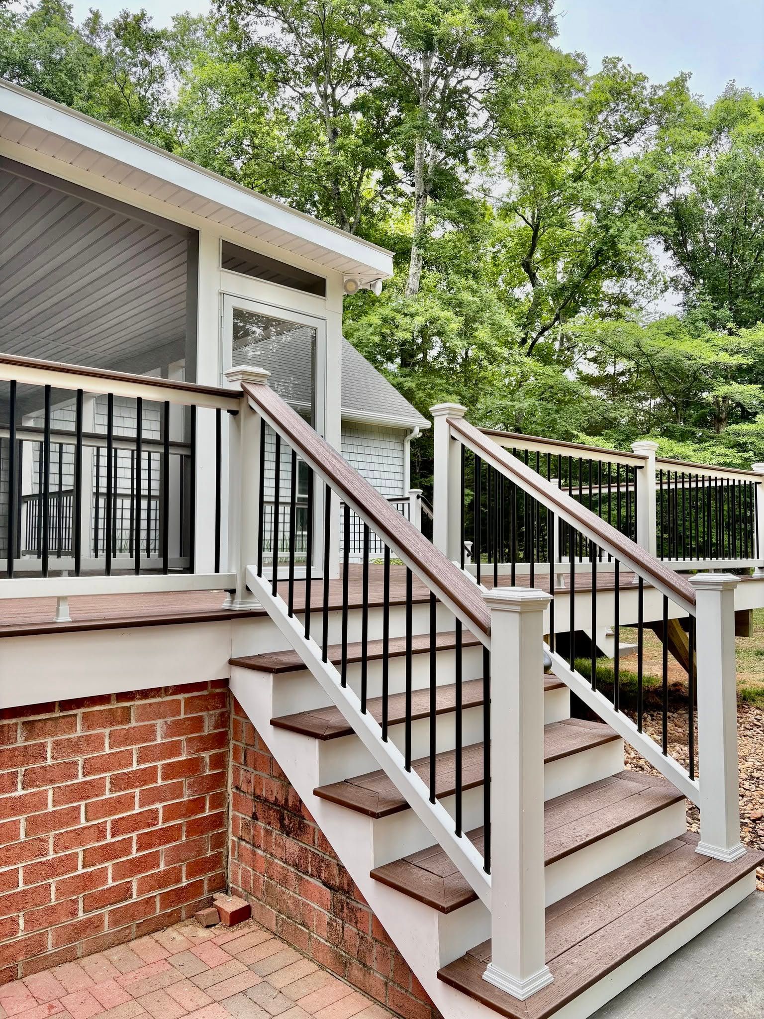 Exterior staircase with white railings and brick base beside a house under trees