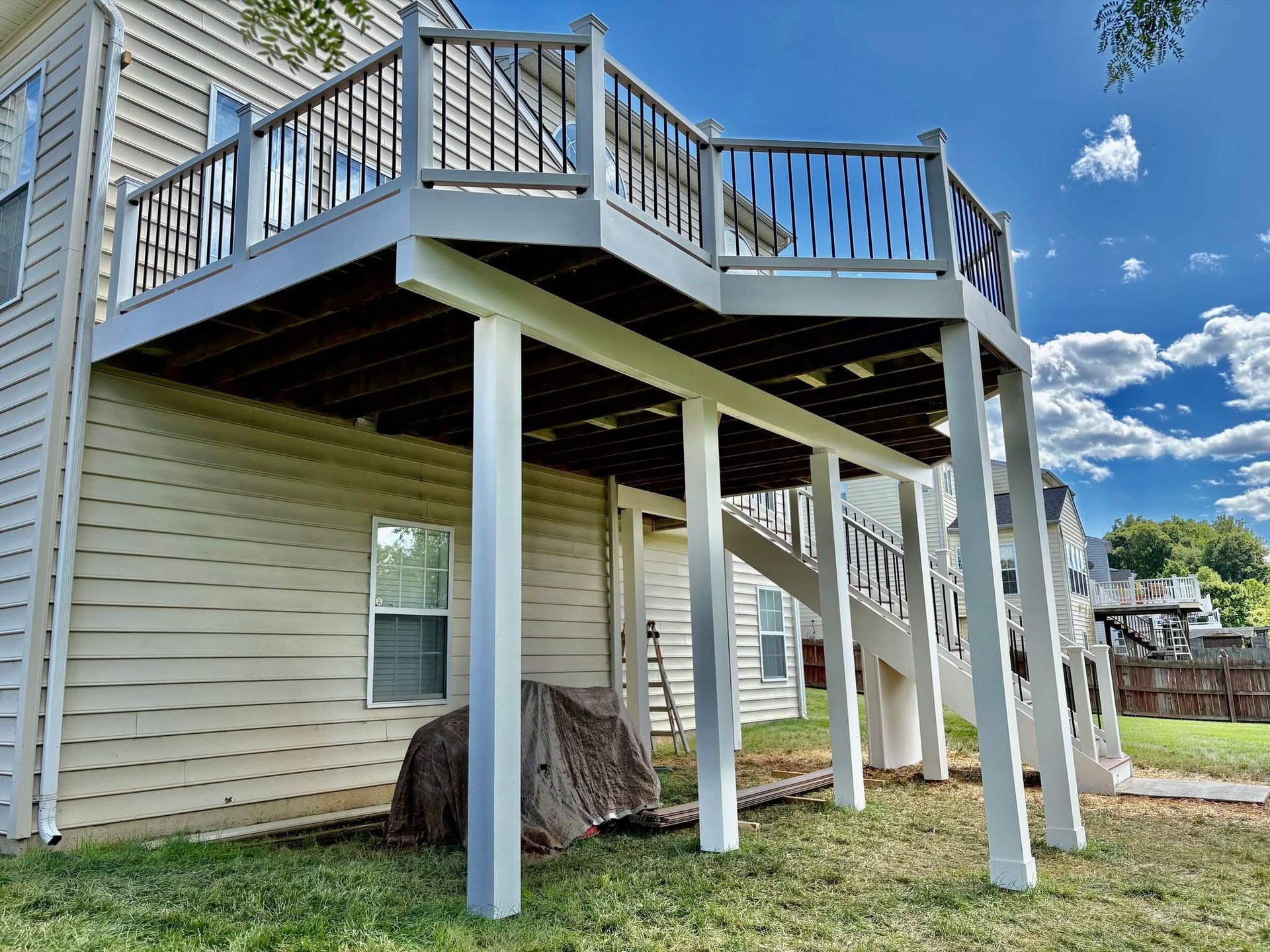 Raised wooden deck with white support posts attached to a beige house under a blue sky