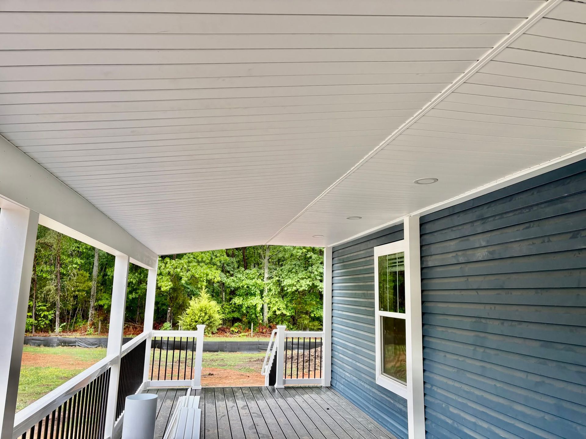 Covered front porch with white ceiling, blue siding, railing, and view of a tree-lined street.