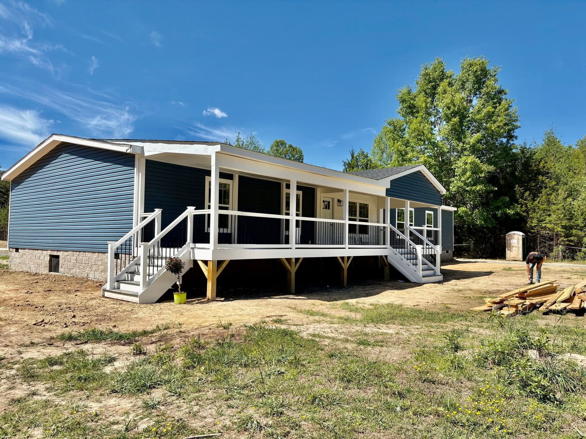 Blue house with a white porch and stairs on a grassy lot under a clear sky