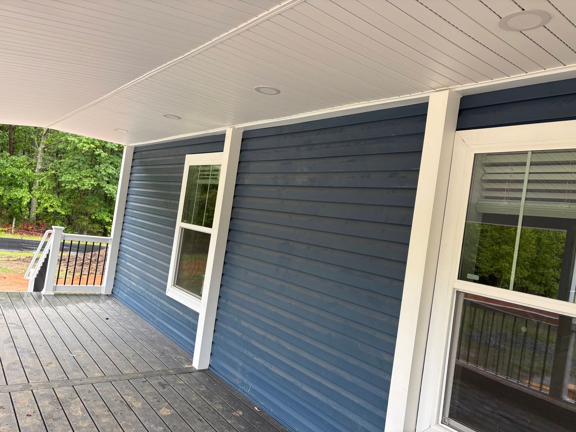 Blue house porch with white trim, wood deck, and windows overlooking trees
