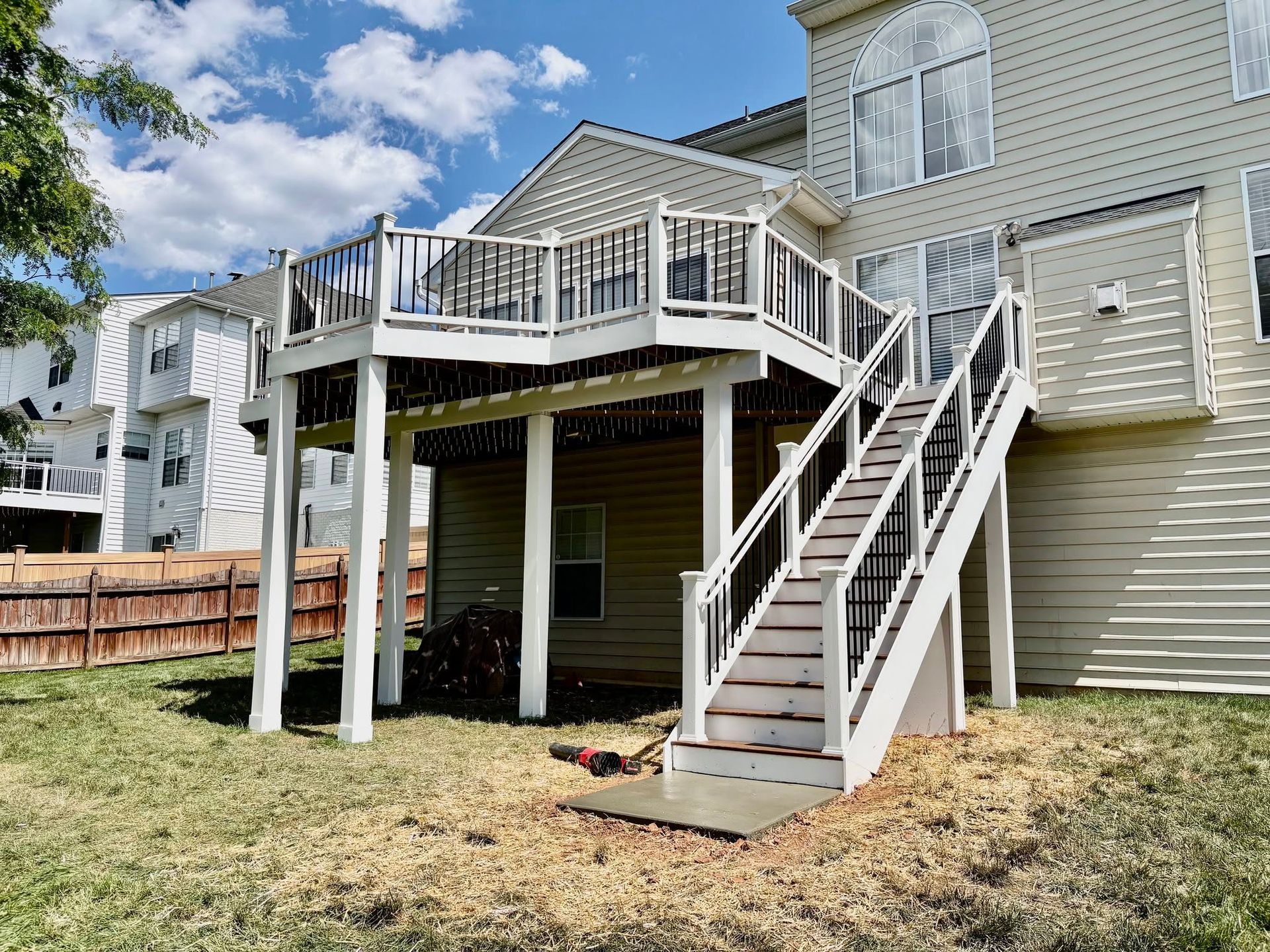 Backyard deck with white stairs and railings attached to a beige house under a blue sky