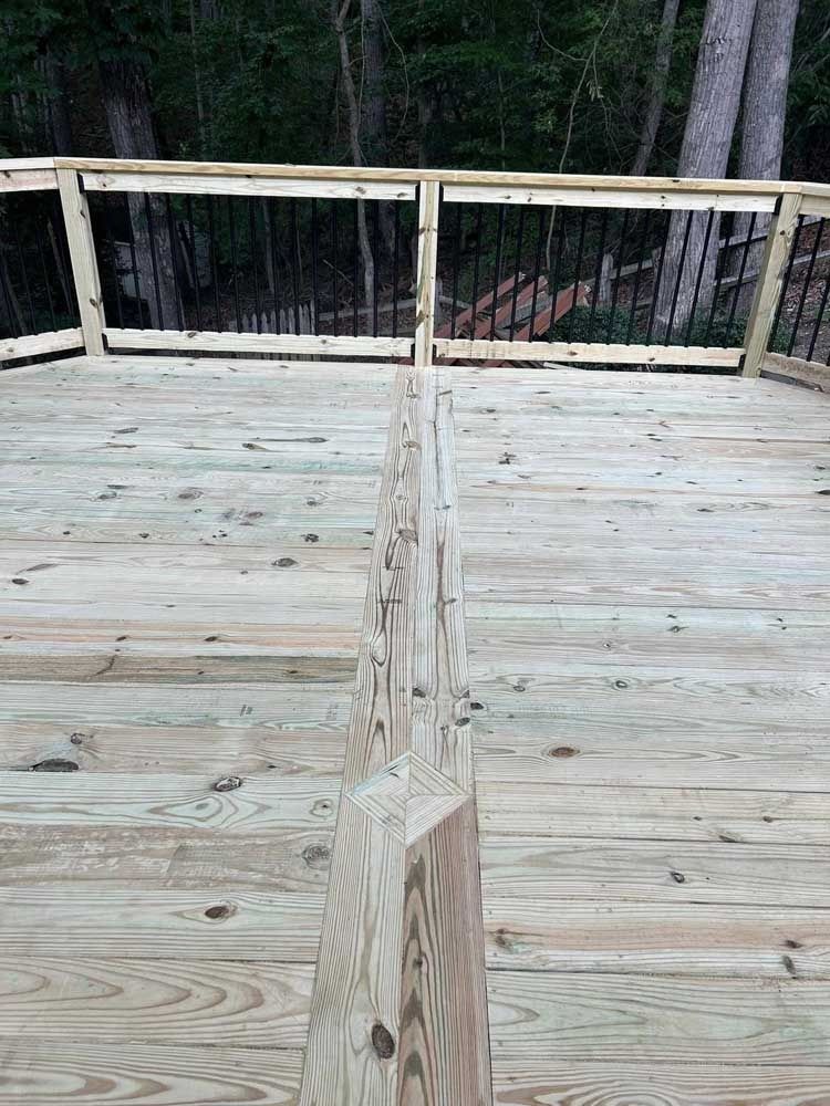 Weathered wooden deck with a split walkway leading to a railing and wooded backdrop