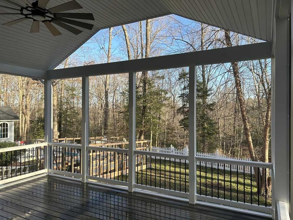 Covered porch with ceiling fan, white railing, and screened panels overlooking trees and a yard