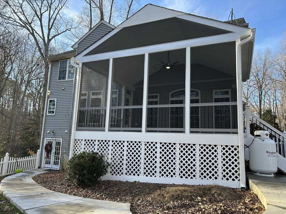 Gray house with screened porch, white lattice skirting, and a propane tank beside leafless trees.