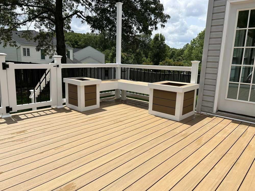 Spacious tan deck with built-in bench seating, white railings, and a view of trees and neighboring houses