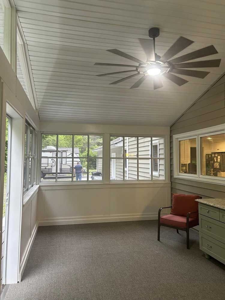 Screened porch with ceiling fan, windows, red chair, and built-in cabinets