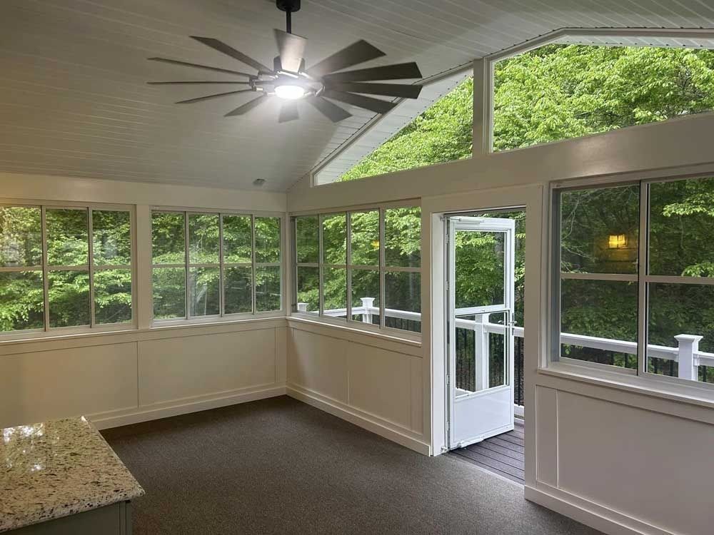 Bright screened sunroom with vaulted ceiling, ceiling fan, windows, and open door to greenery