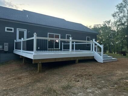 White wooden deck with railings attached to a dark gray house in a yard at dusk