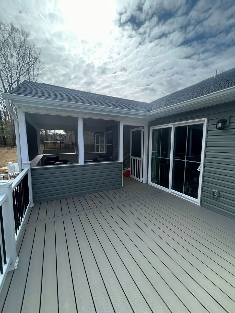Covered wooden deck with gray siding, sliding glass doors, and a pergola under a cloudy sky