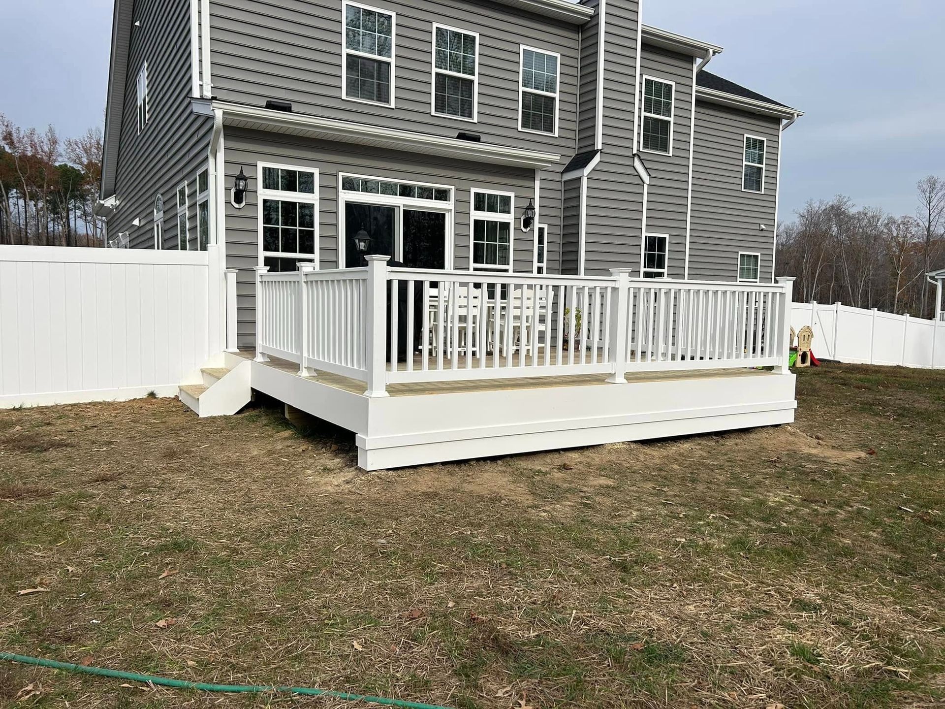 Backyard deck with white railing attached to a gray two-story house