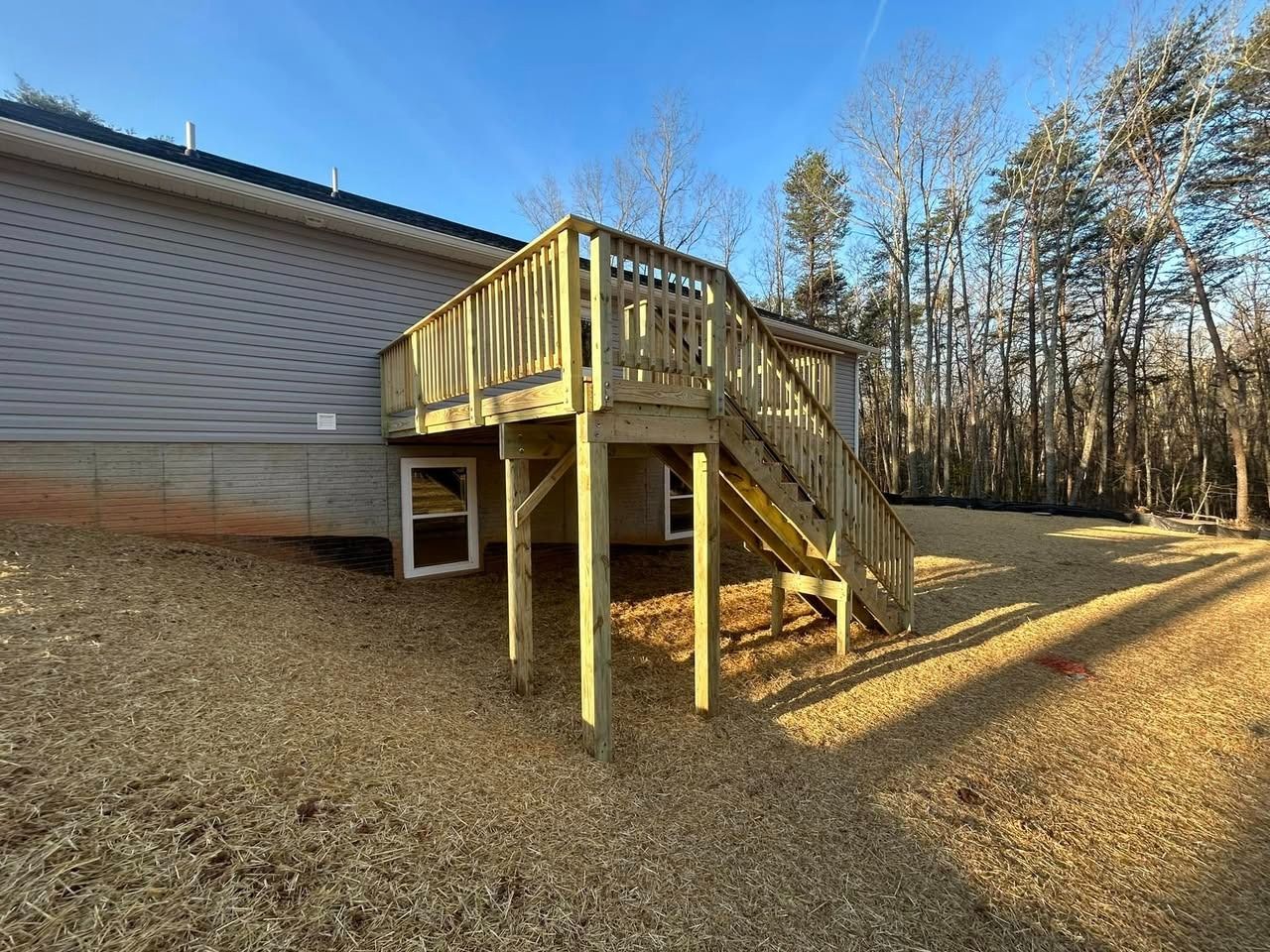 Wooden deck and stairs attached to a house beside a wooded yard in winter