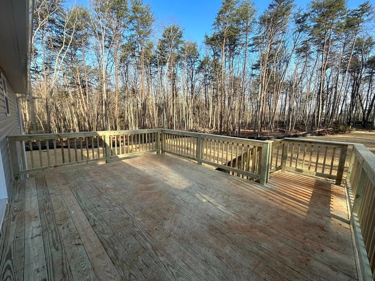 Wooden deck with railing overlooking a wooded area on a sunny day