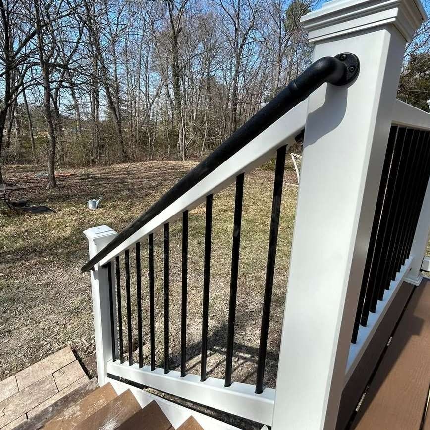 Black metal railing on a white porch staircase beside a wooded yard.