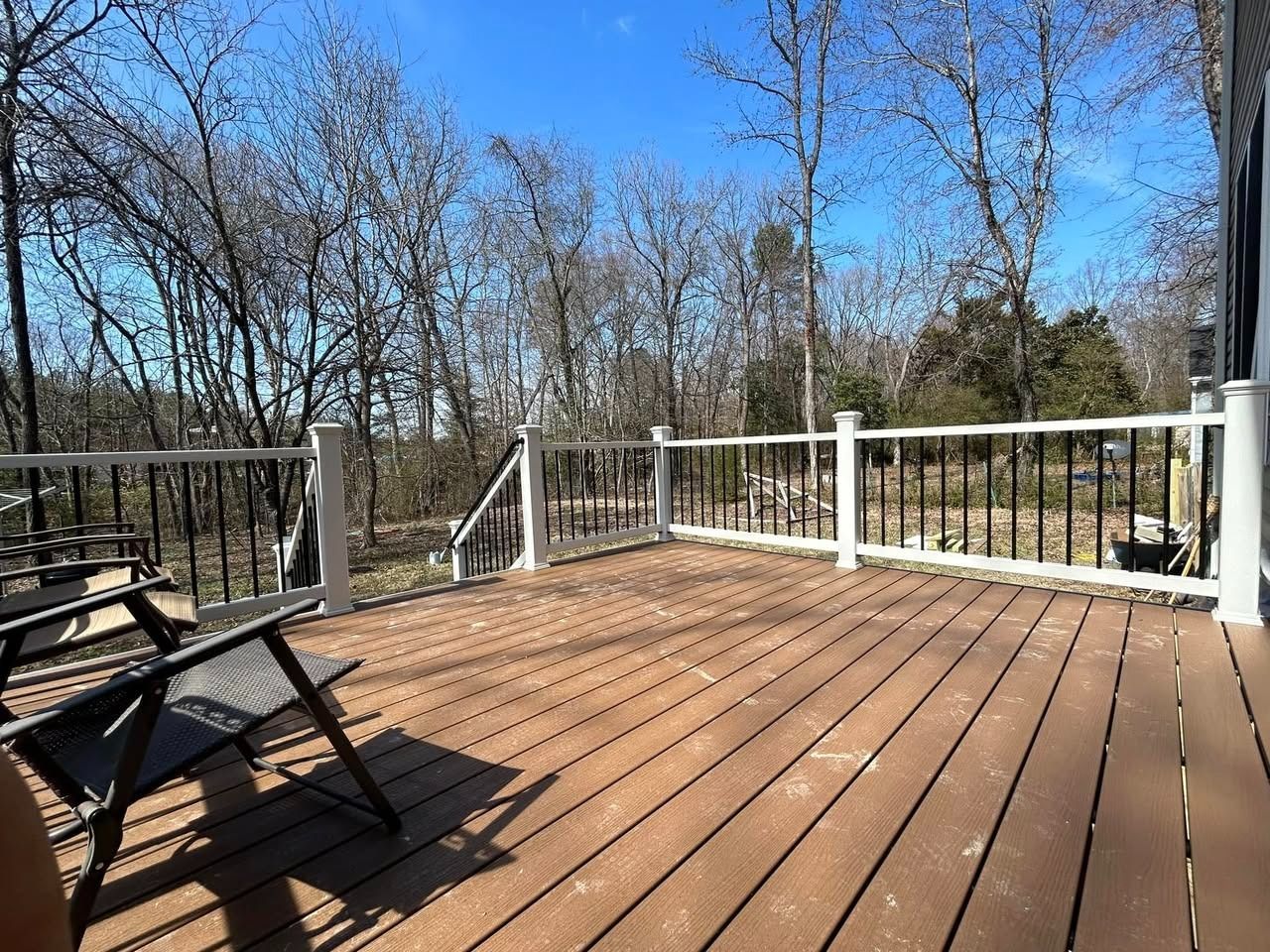 Wooden deck with white railing and chairs overlooking leafless trees under a clear blue sky