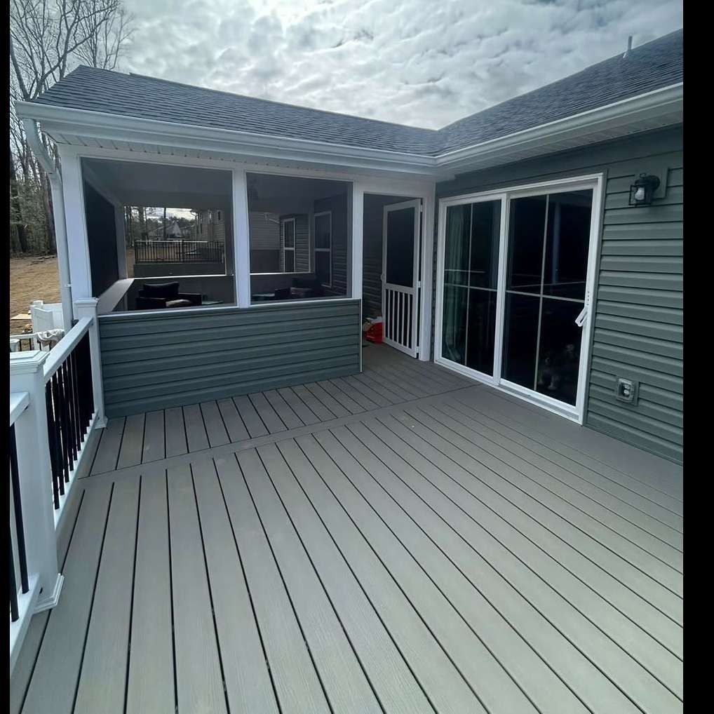 Covered gray deck with white railings and sliding glass doors beside a house