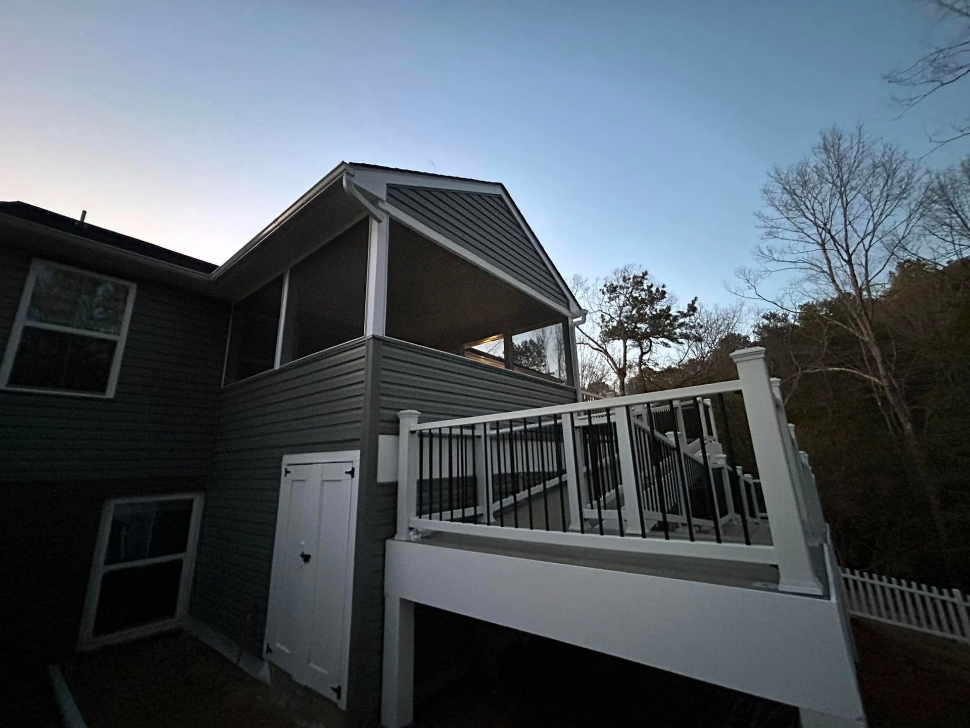 House exterior with white deck and railings beside a sloped roof at dusk