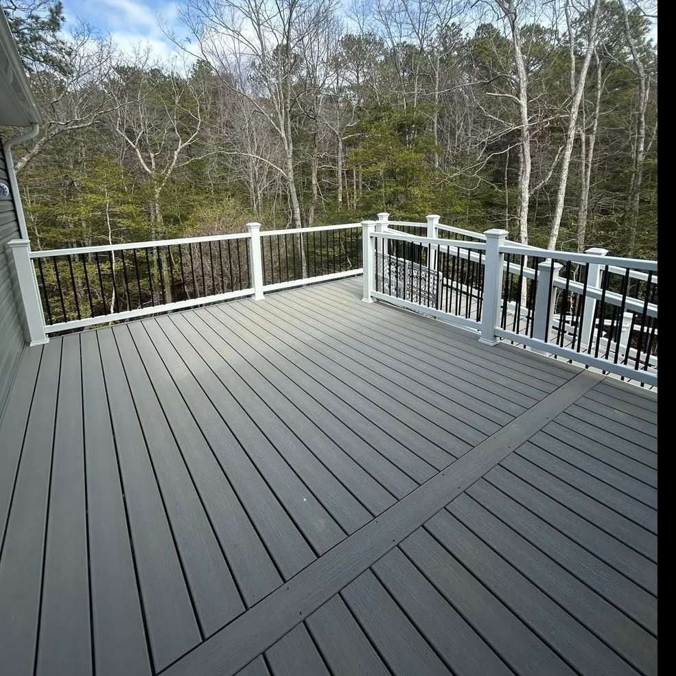 Gray deck with white railing overlooking wooded trees and a pool