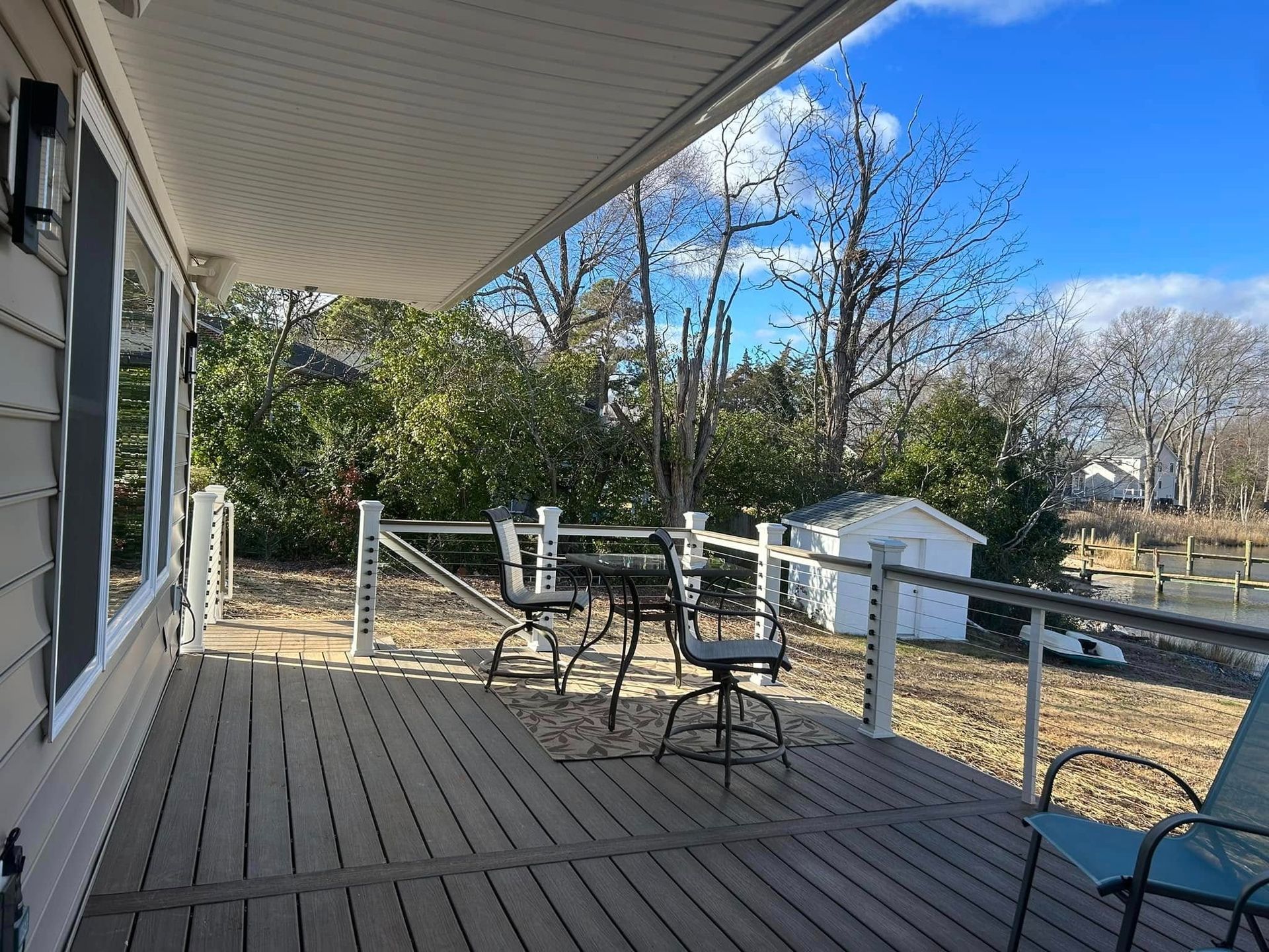 Covered wooden porch with metal chairs, railing, and a yard with leafless trees beyond.