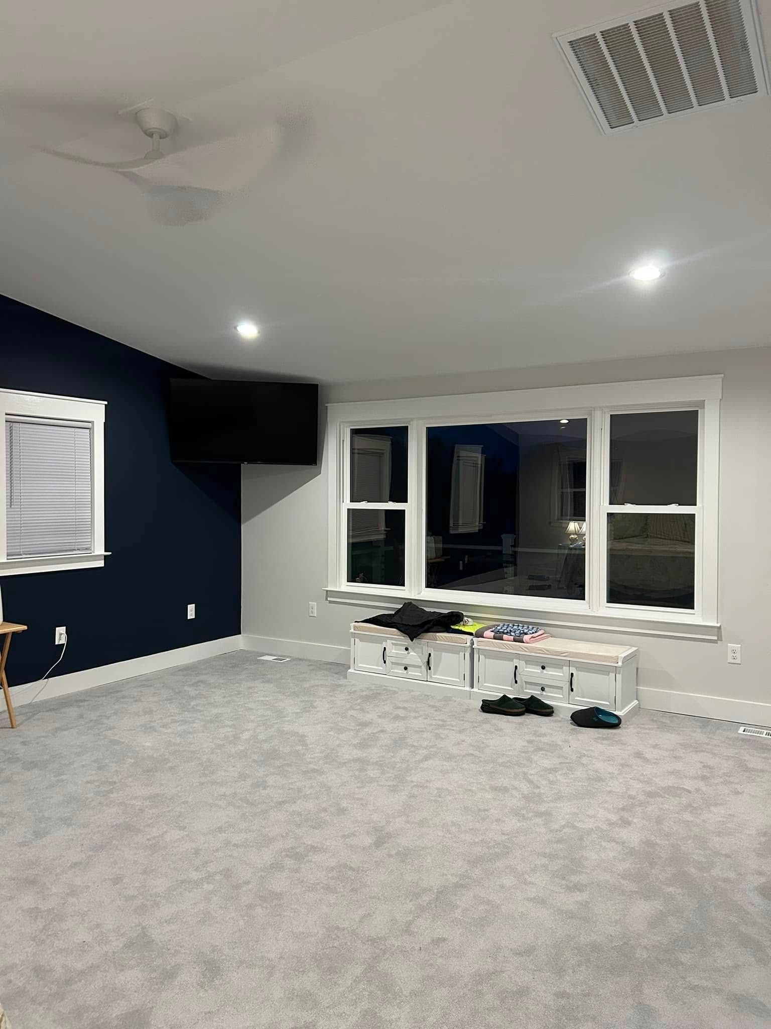 Empty carpeted living room with dark accent wall, large windows, and ceiling lights turned on