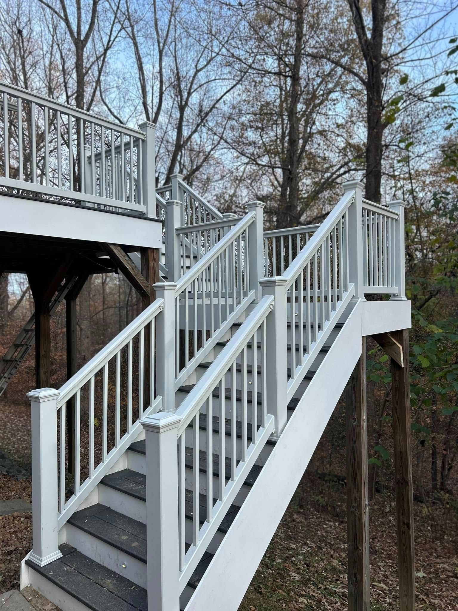 White outdoor staircase with railings leading up to a deck in a wooded yard