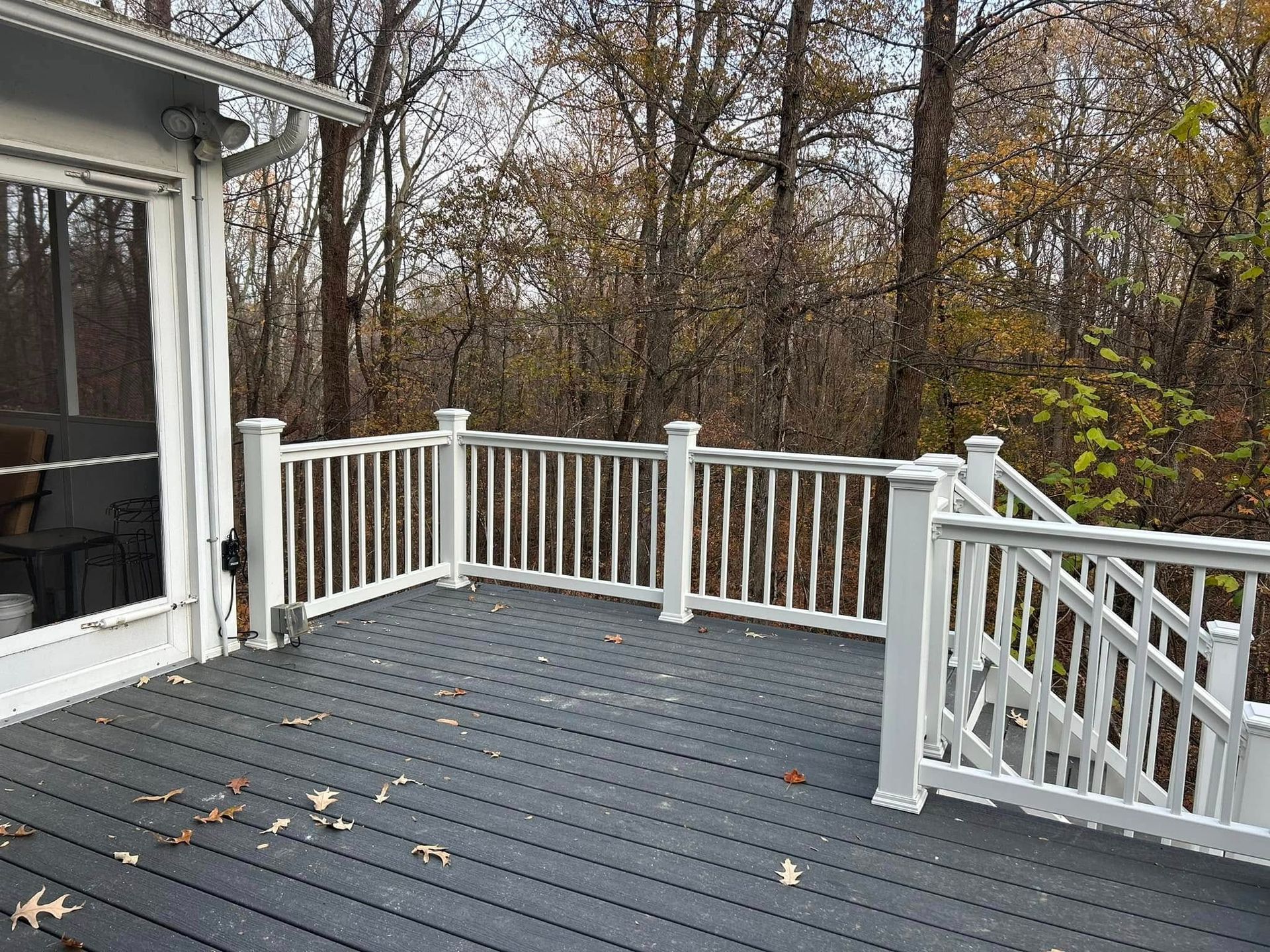 Empty gray deck with white railings overlooking autumn trees