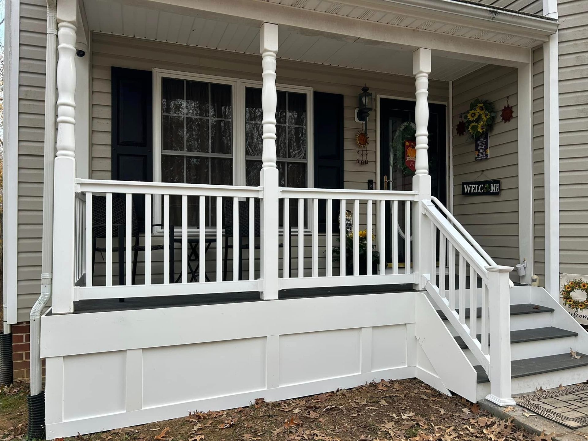 Front porch with white railing and steps, gray siding, black shutters, and hanging flowers.