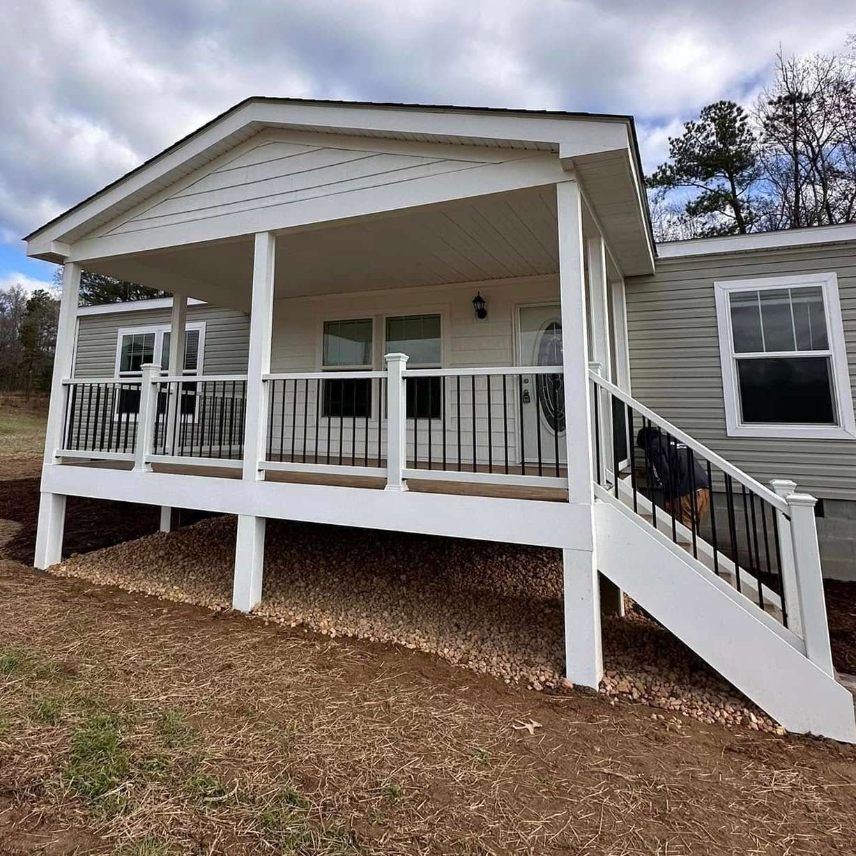 White porch on a gray house with stairs and black railings, set on a wooded lot.