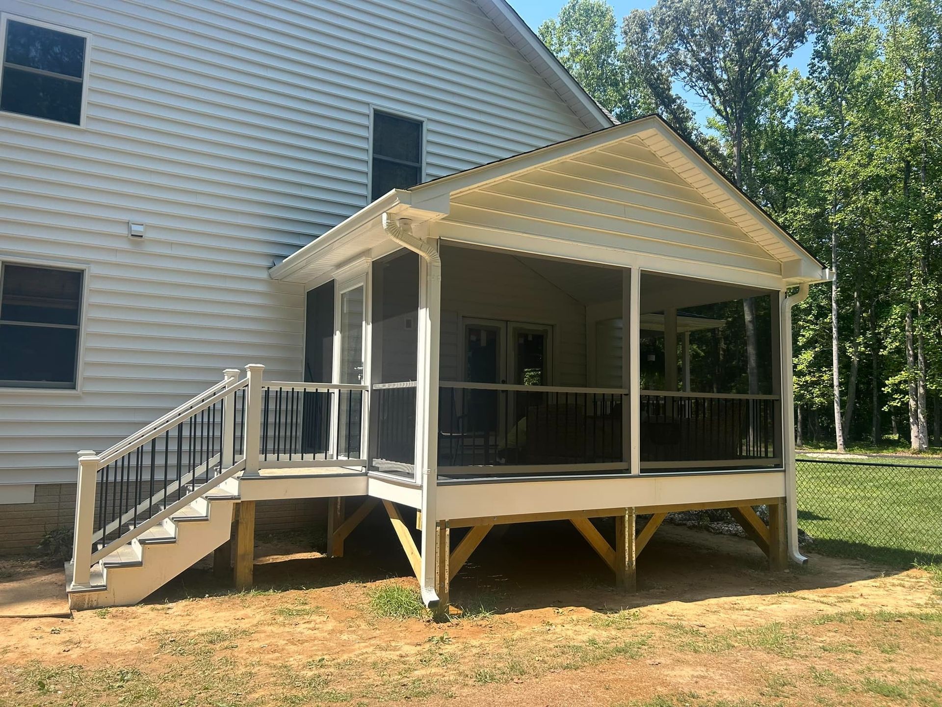 White house with a screened porch, steps, and wooden support posts in a wooded yard.