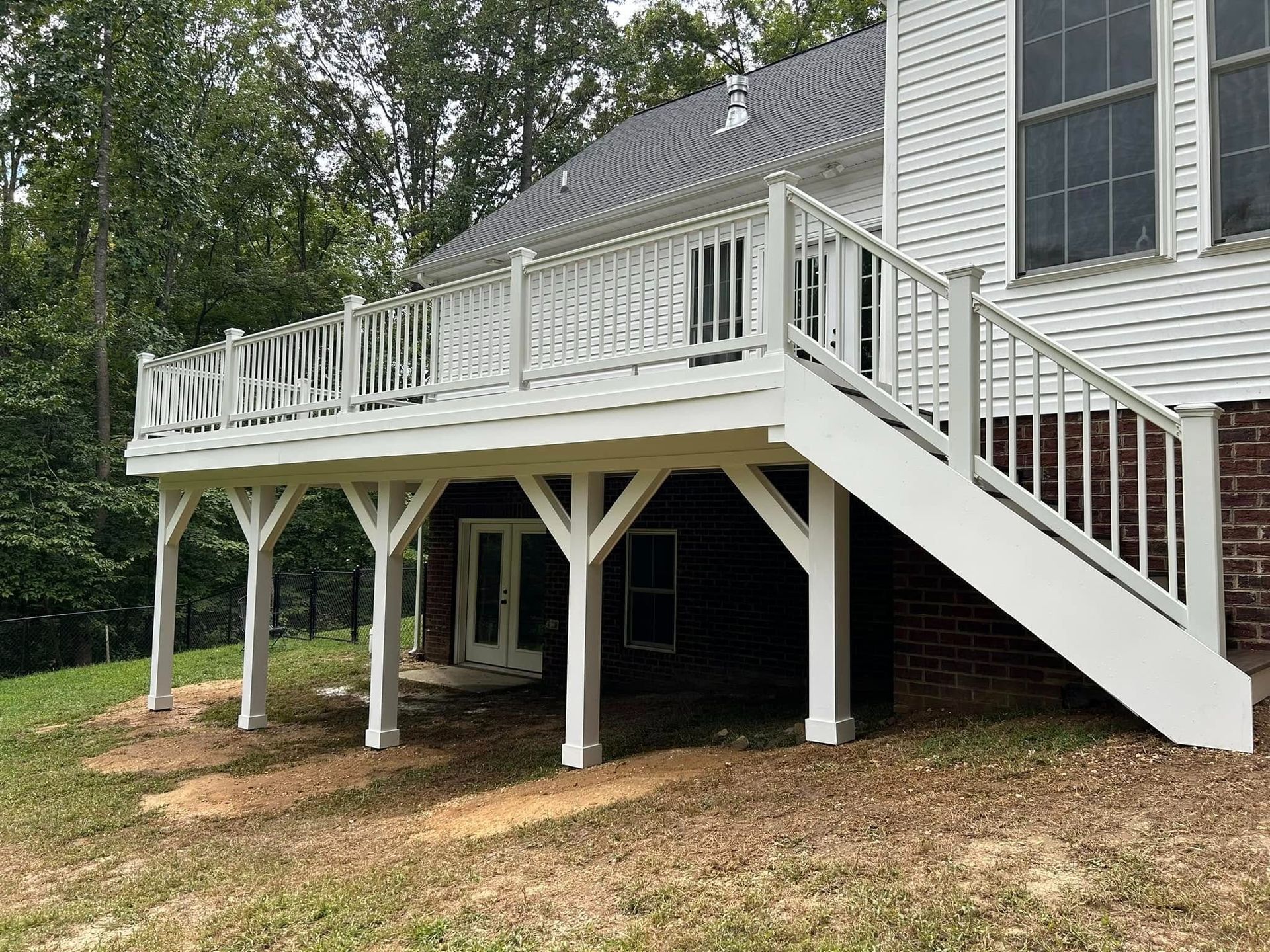Raised white deck with stairs attached to a gray house in a wooded yard