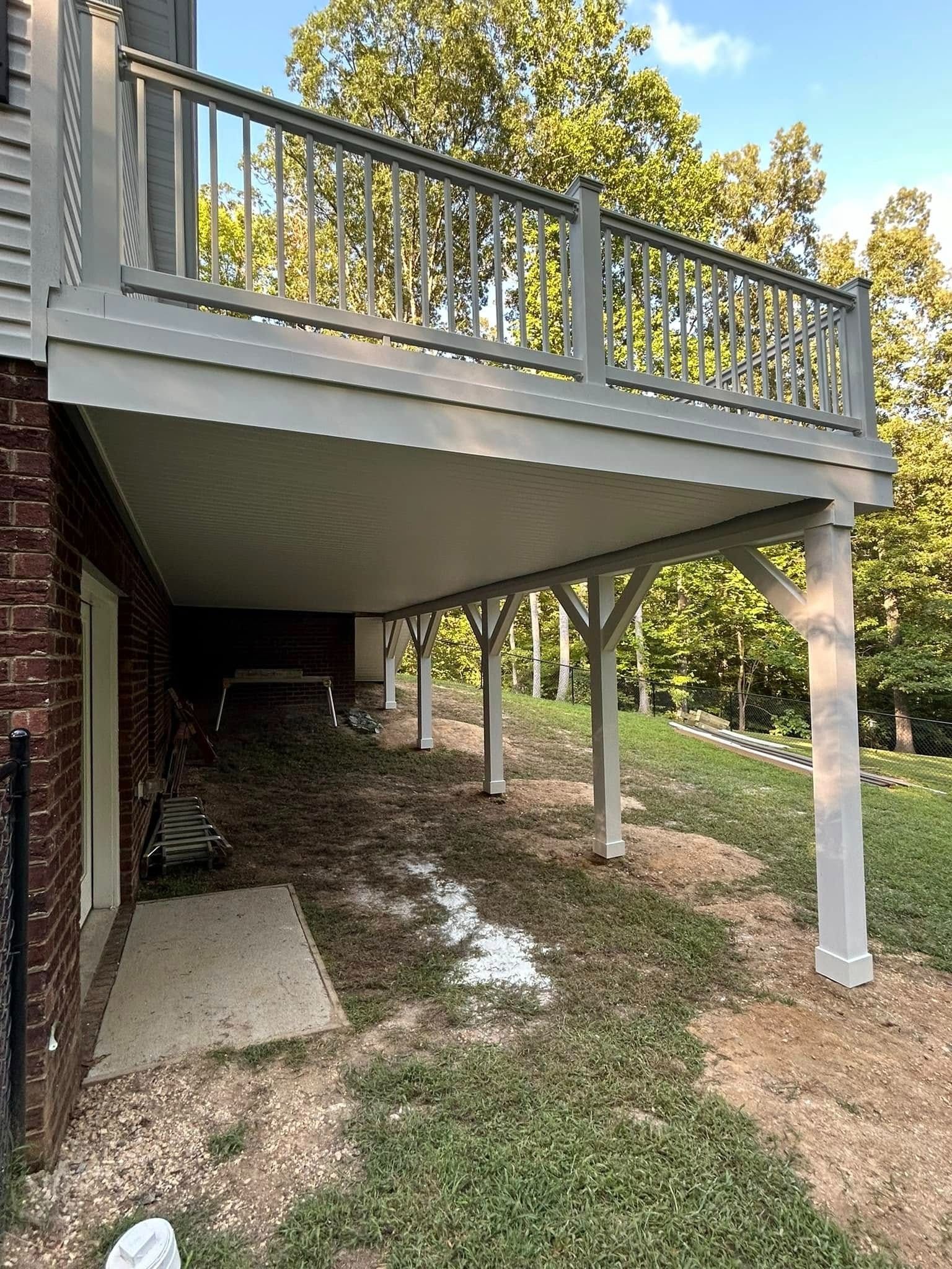 Elevated deck with gray railing and white support posts over a shaded backyard area