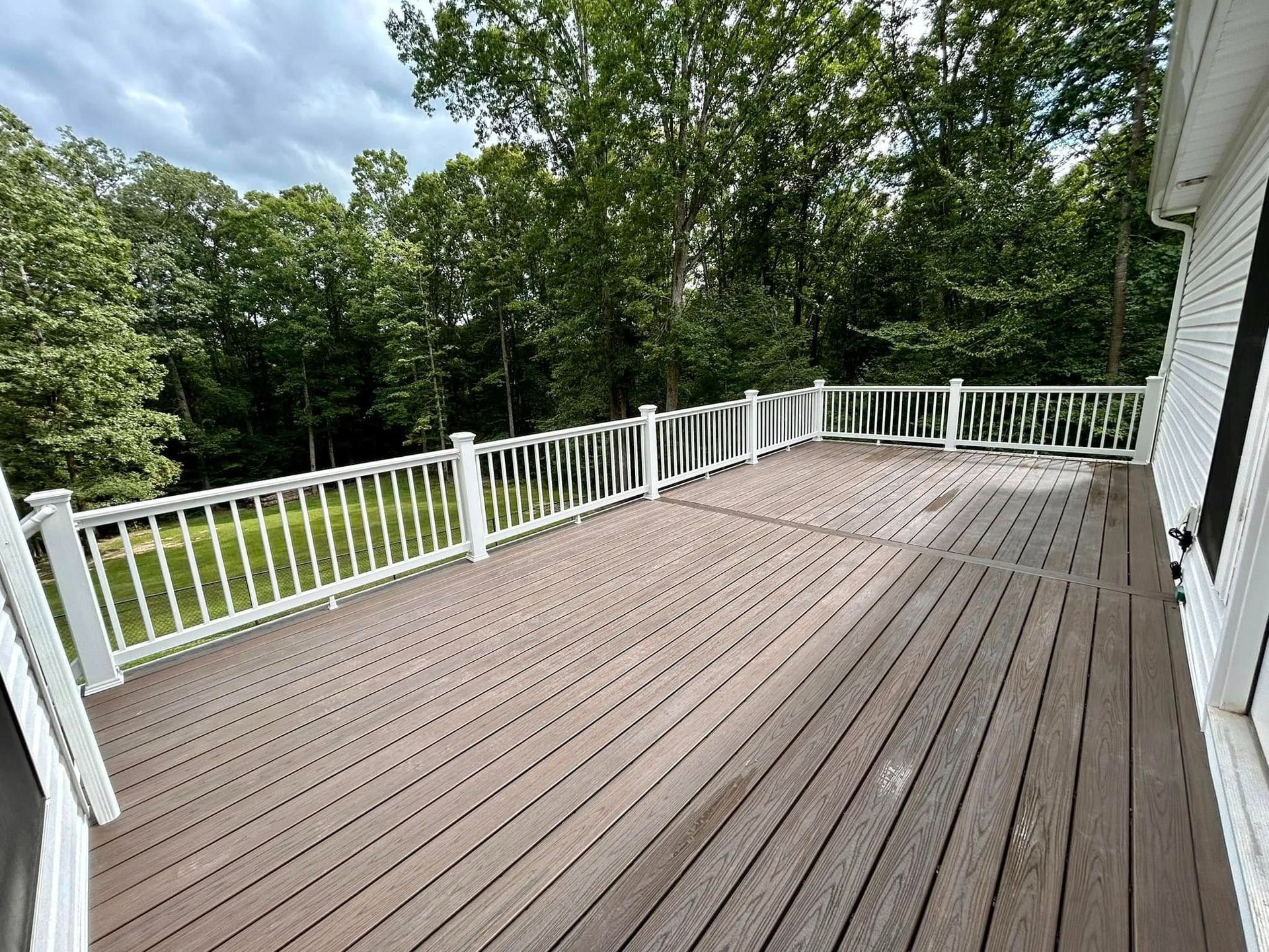 Large wooden deck with white railing overlooking a green wooded yard