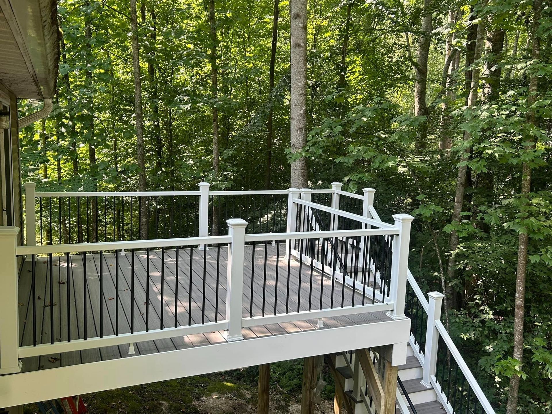 Wooden deck with white railings beside a forested hillside
