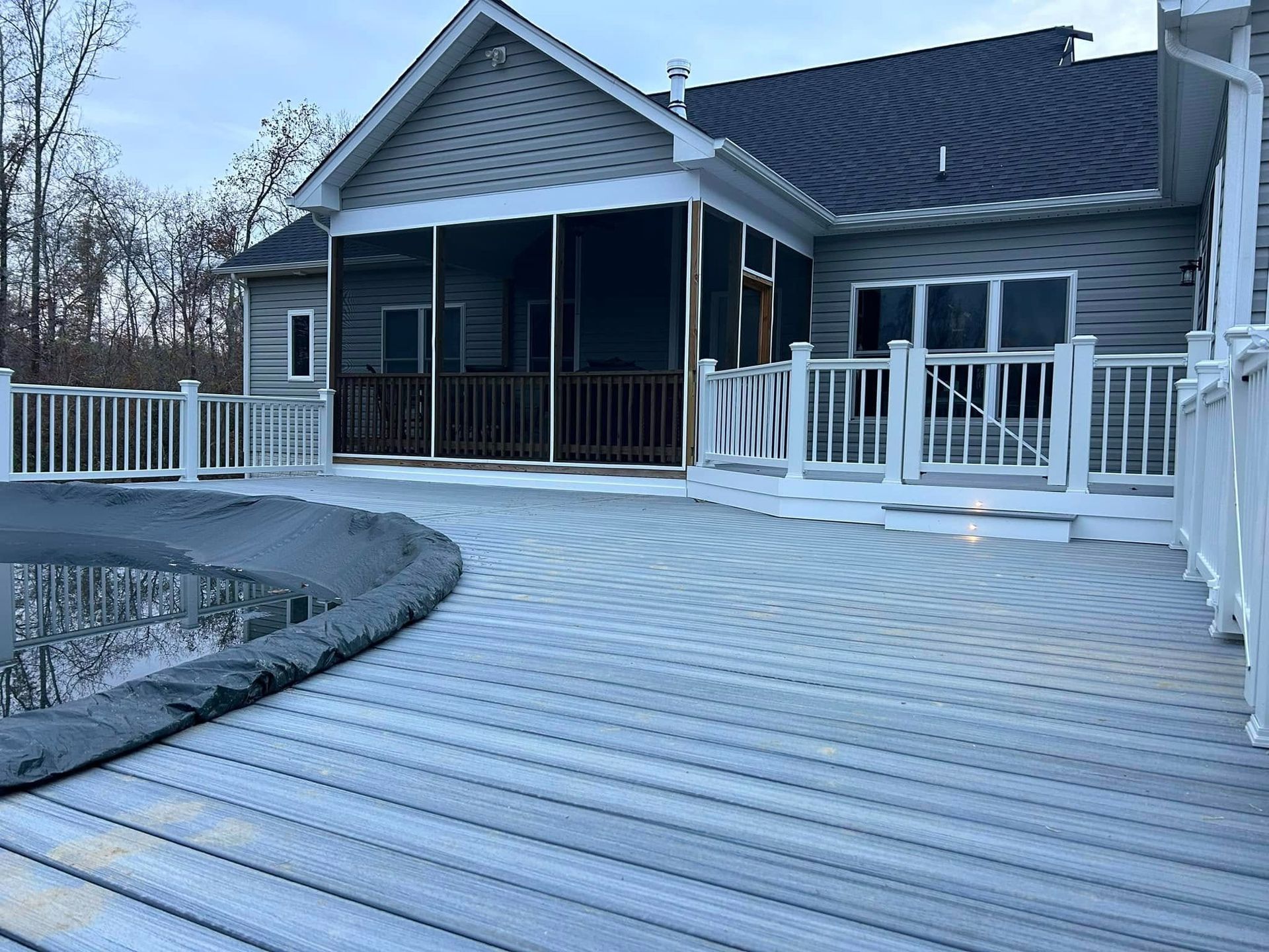 House with a curved wooden deck and screened porch by a pond, viewed in winter.