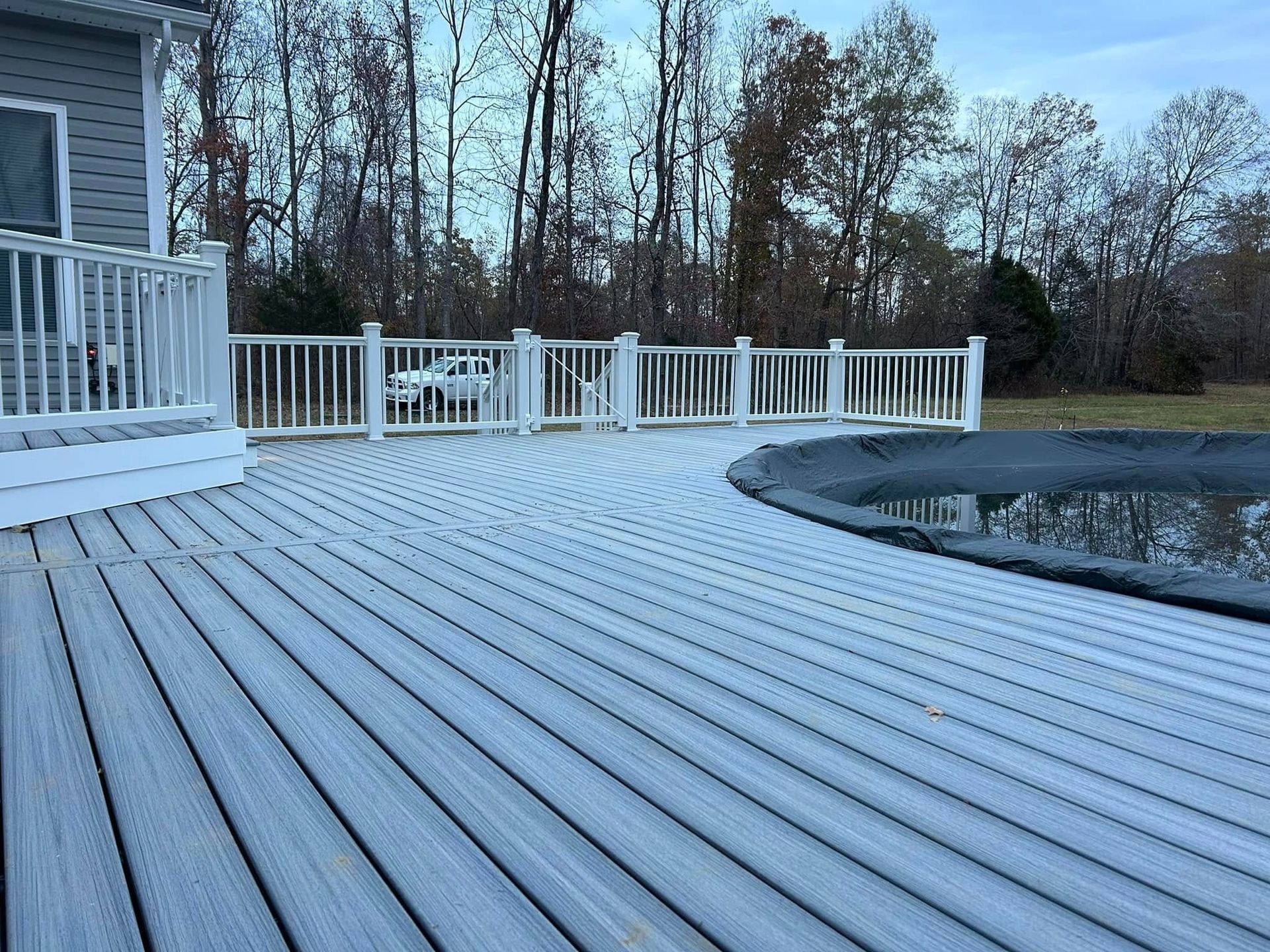 Snow-covered wooden deck curving around an above-ground pool beside a house and white railing