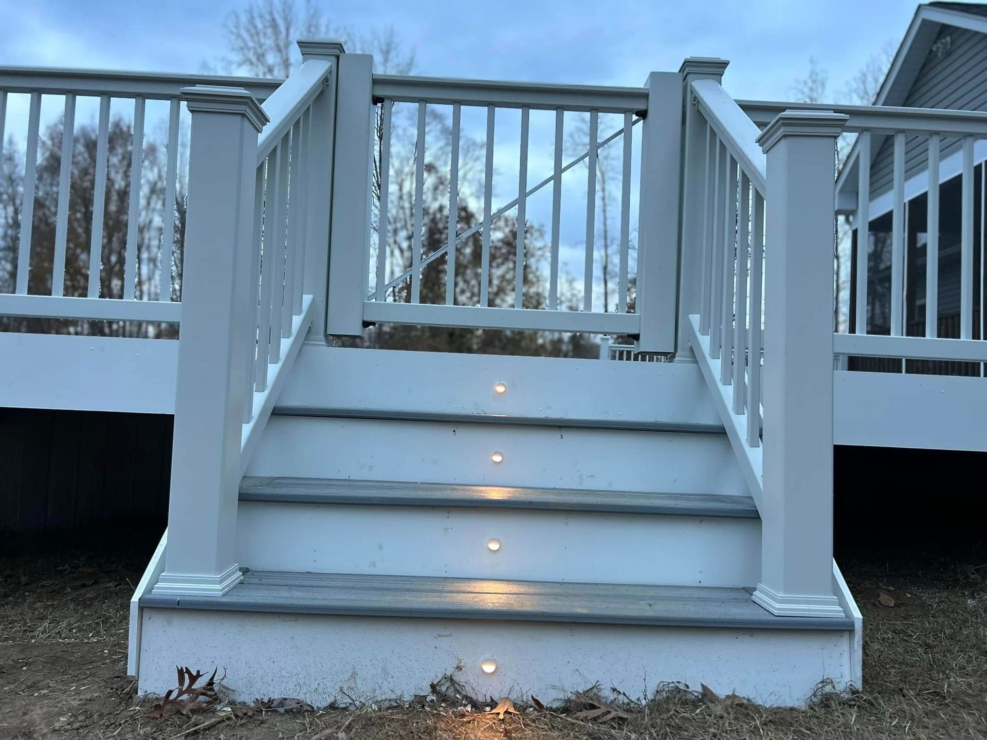 White outdoor stairs with railings and small step lights, leading to a deck in snowy weather