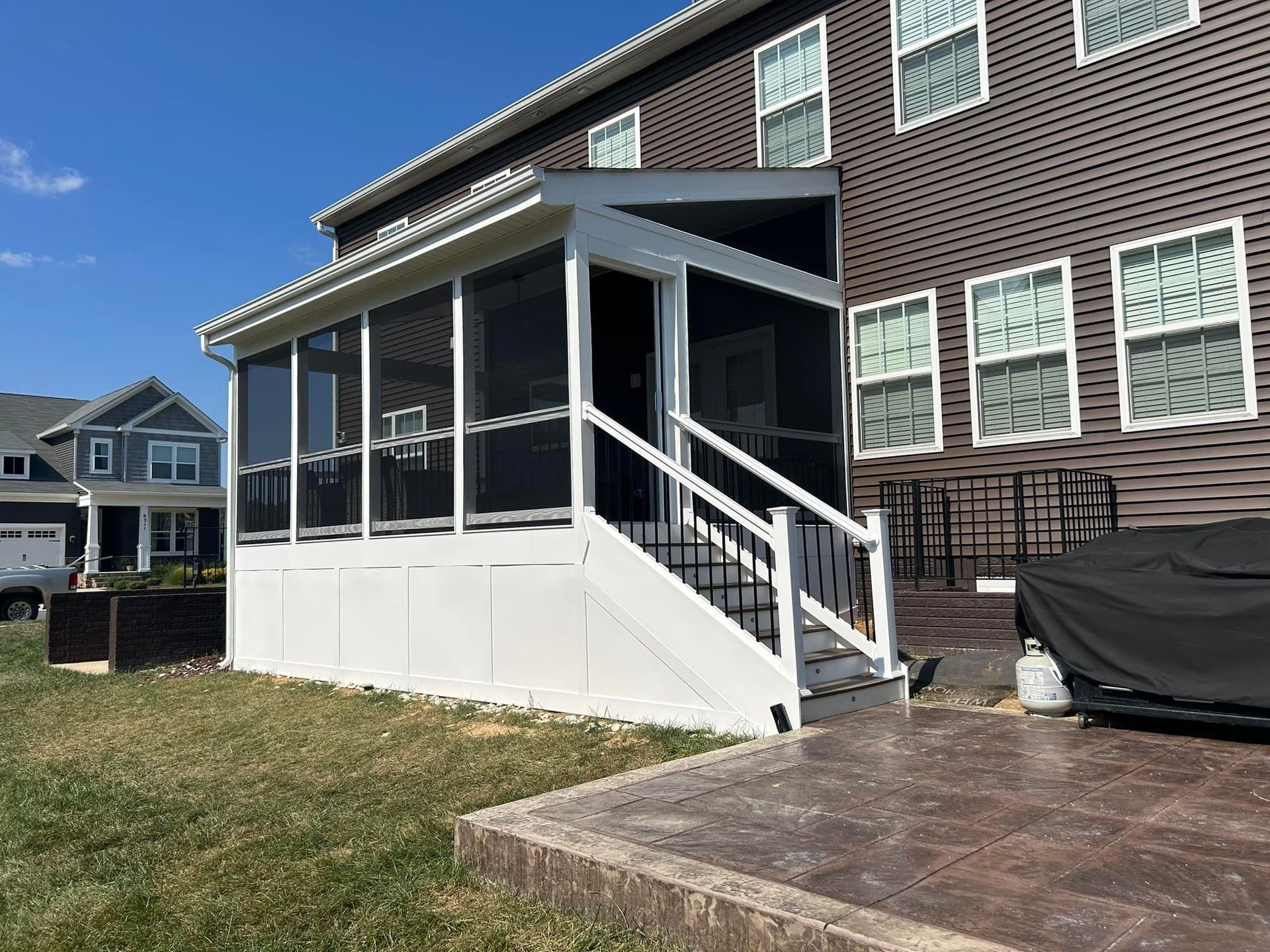 Screened porch with white stairs attached to a brown house beside a grassy yard