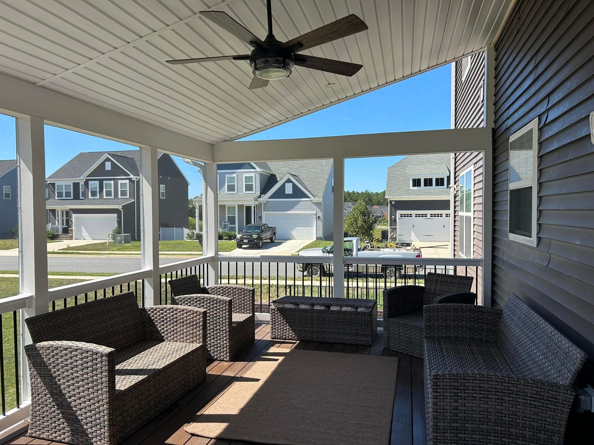 Covered front porch with wicker seating, ceiling fan, and view of suburban houses across the street