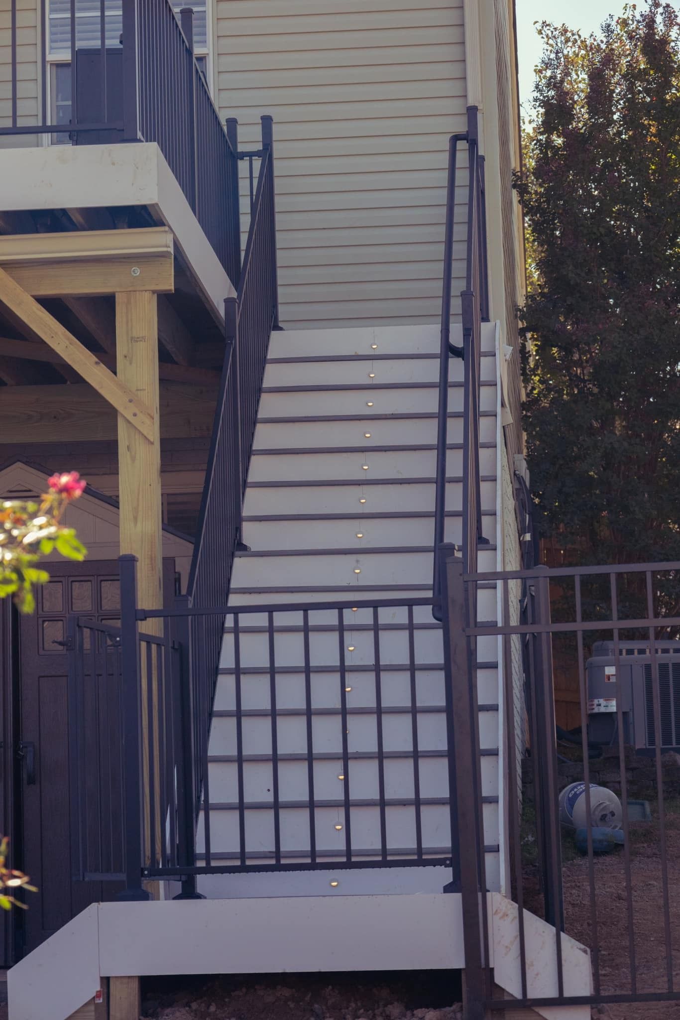 Exterior stairway leading to a raised deck beside a beige house, with black railings and a gated fence.